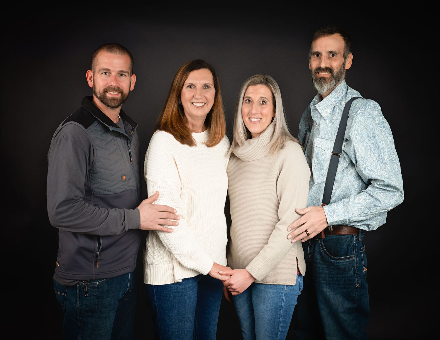Studio portrait of two couples against dark background wearing casual attire.
