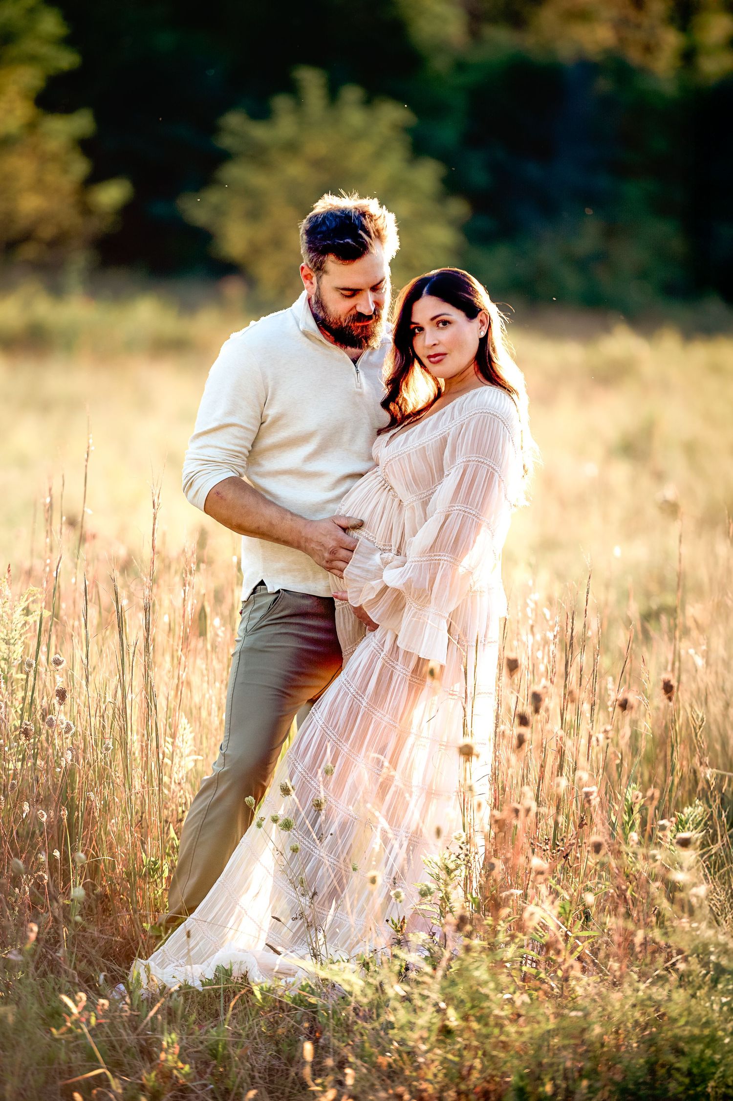 Romantic couple photoshoot in a sunlit field with flowing white dress.