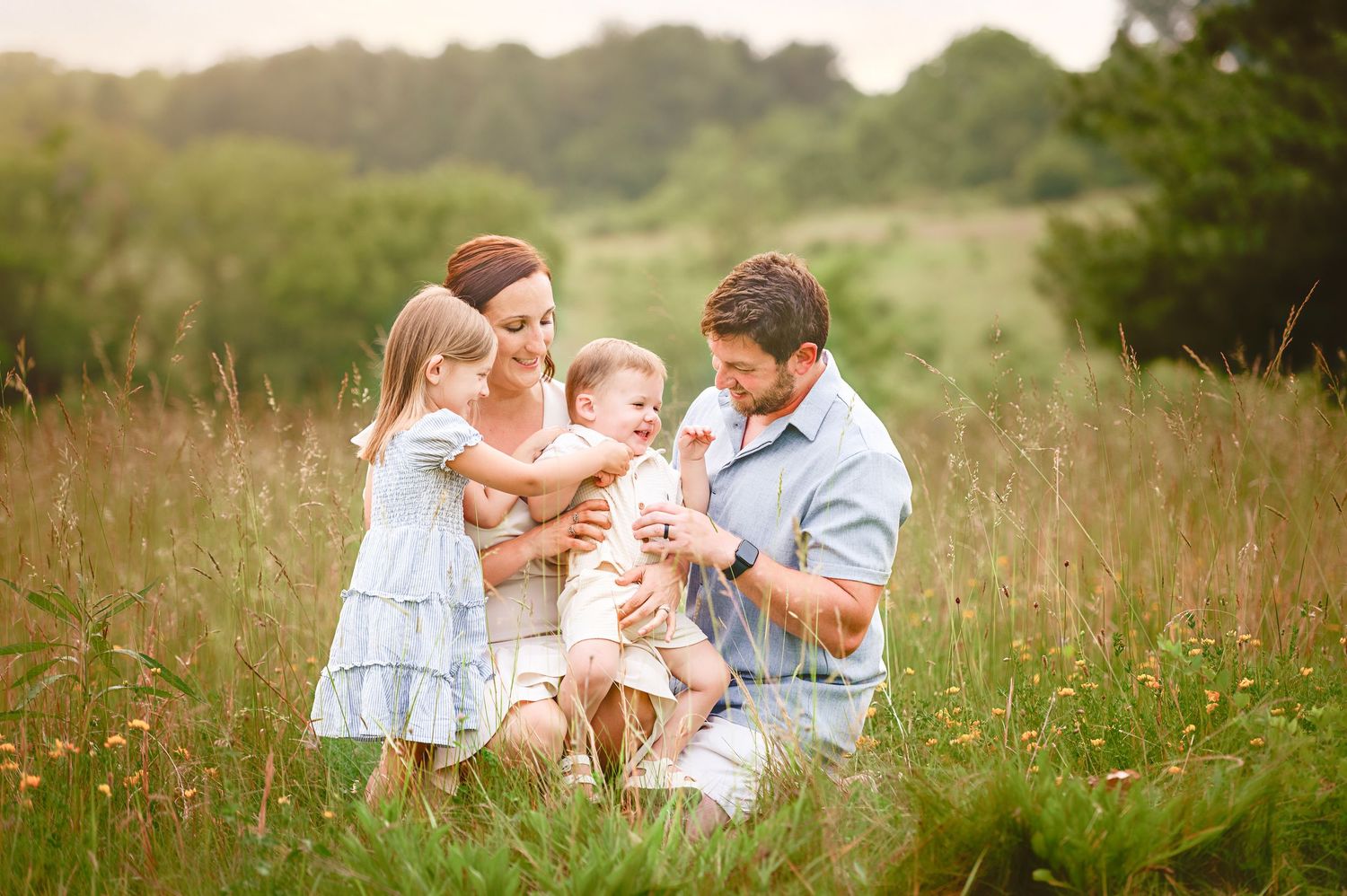 A family shares a tender moment together in a sunlit meadow filled with wildflowers on a warm summer evening.