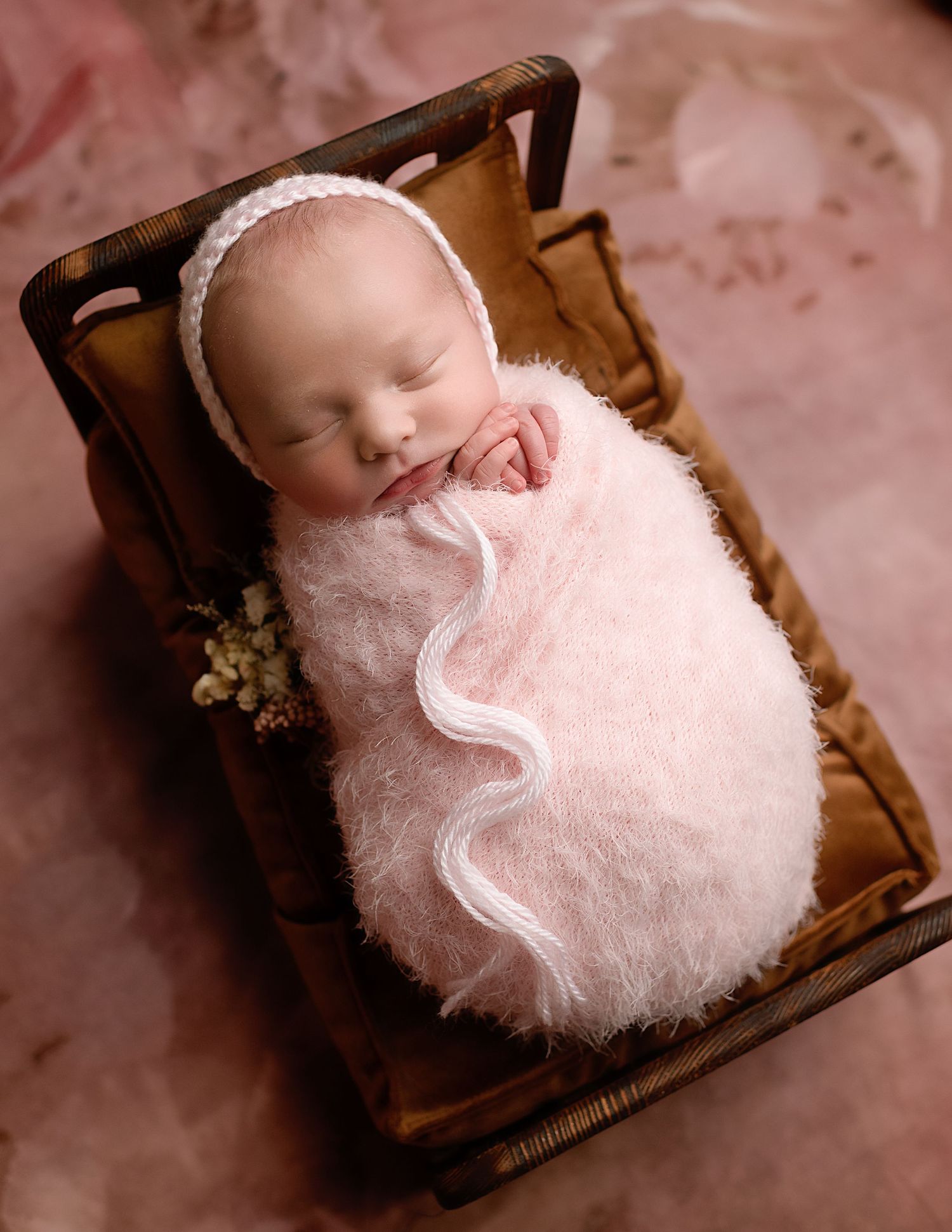 Series of newborn portraits with baby nestled in pink fluffy blankets in wooden boxes.