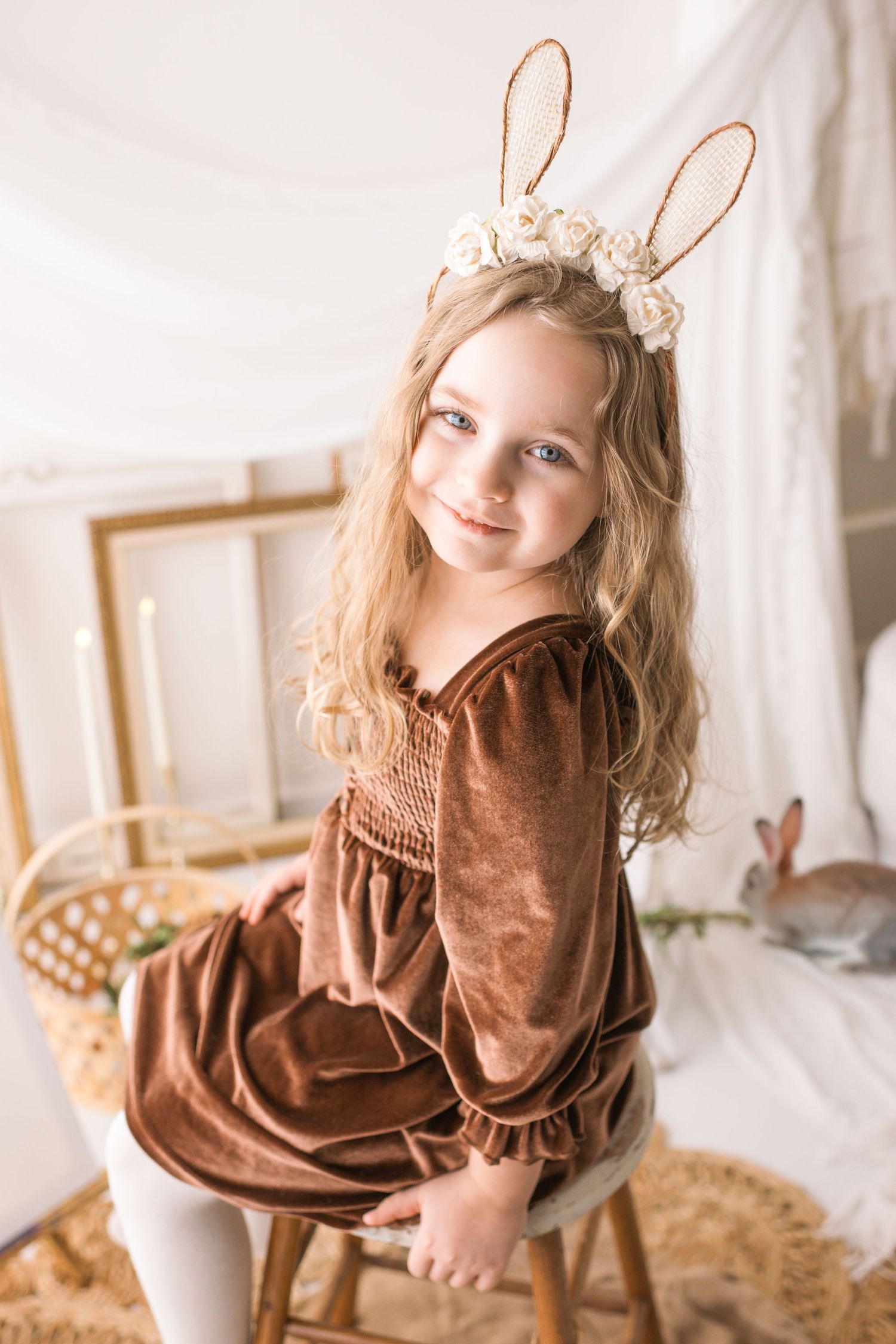 A child in a brown dress sits in a bright, airy room with white decor and natural lighting.
