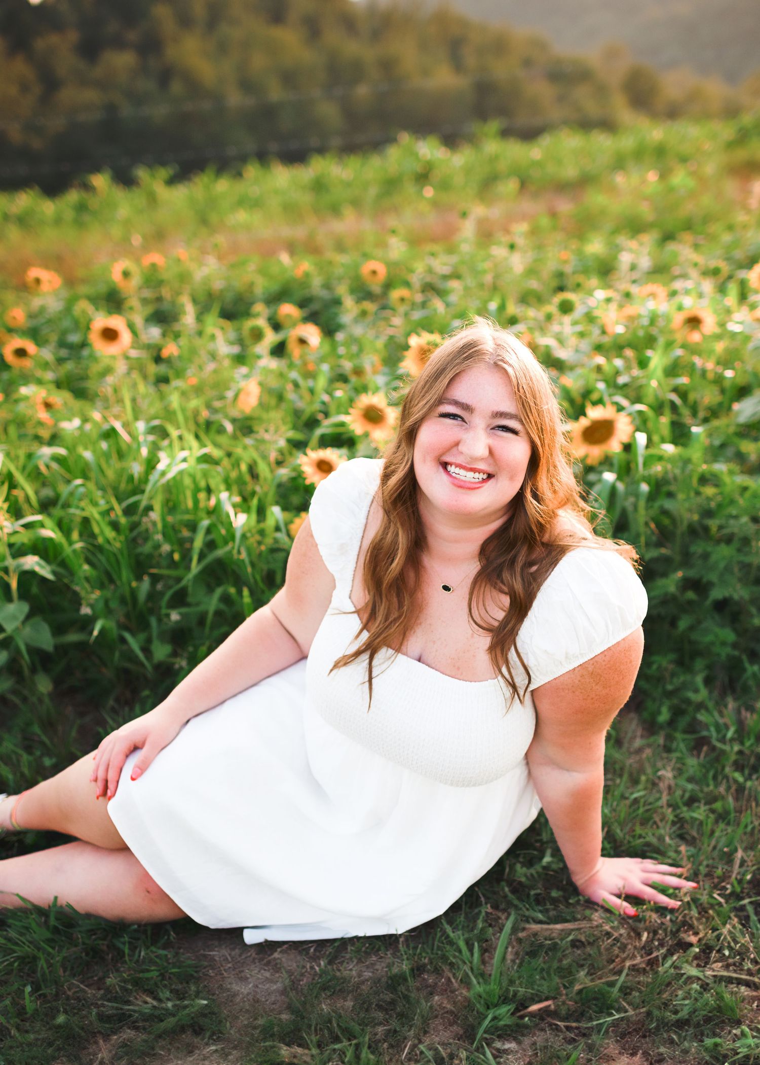 Person in white dress lying playfully in a sunflower field during golden hour.