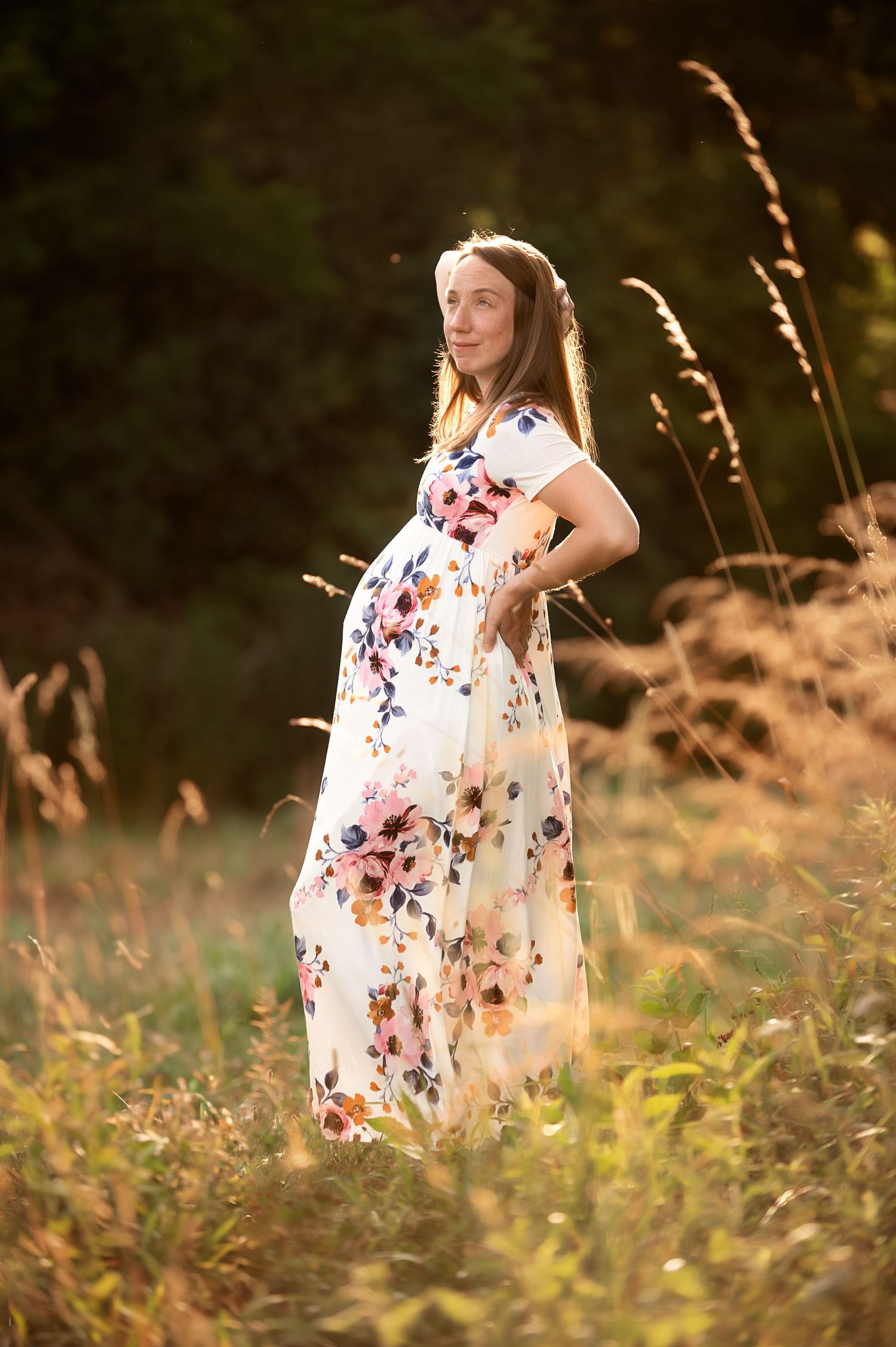 A woman in a floral dress stands in a golden field during sunset.