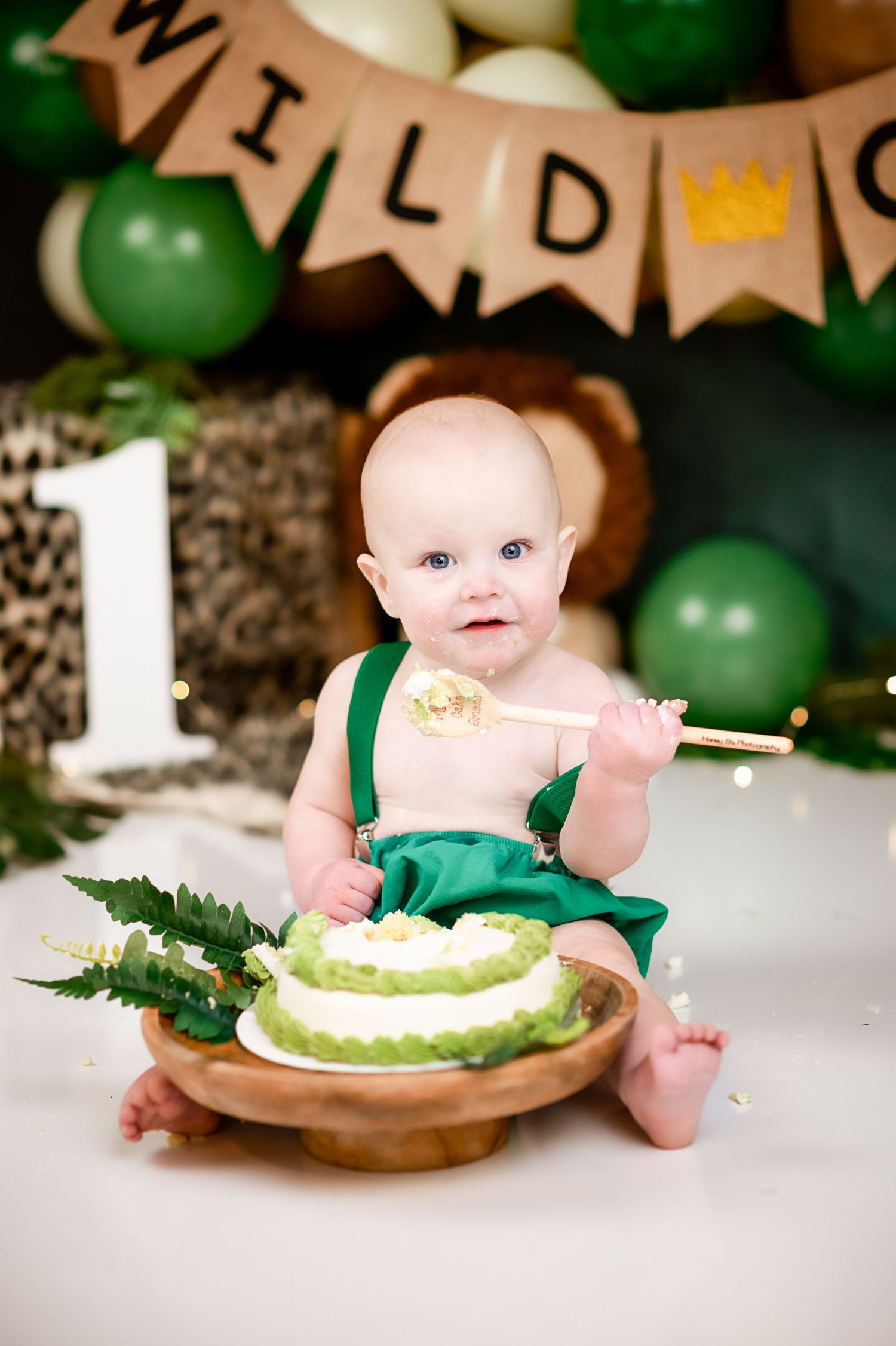 A cake smash setup with green balloons and rustic decorations featuring a small white cake.
