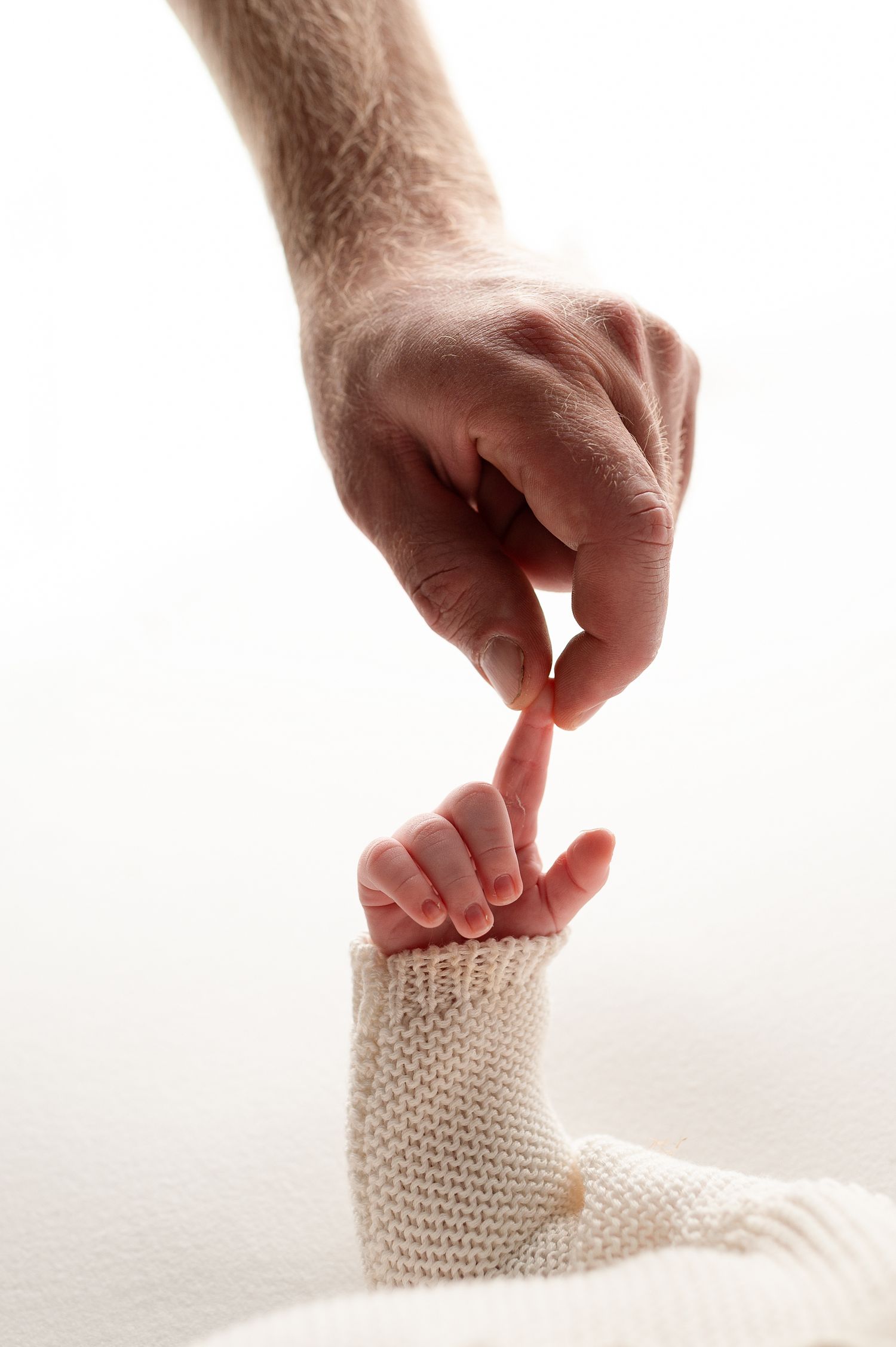 Series of hands gently touching white knit baby booties against bright background.