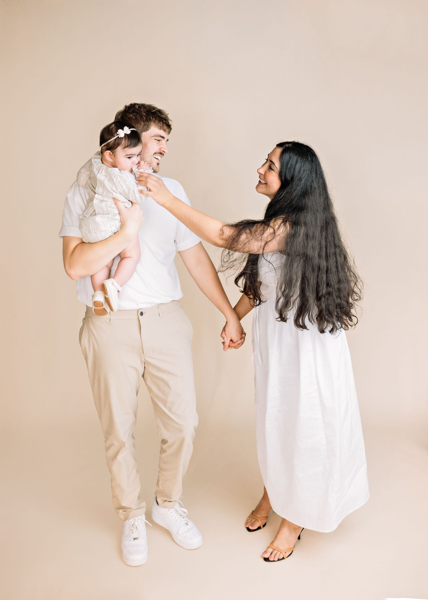 A playful family photo session with everyone wearing white and beige against a neutral background.