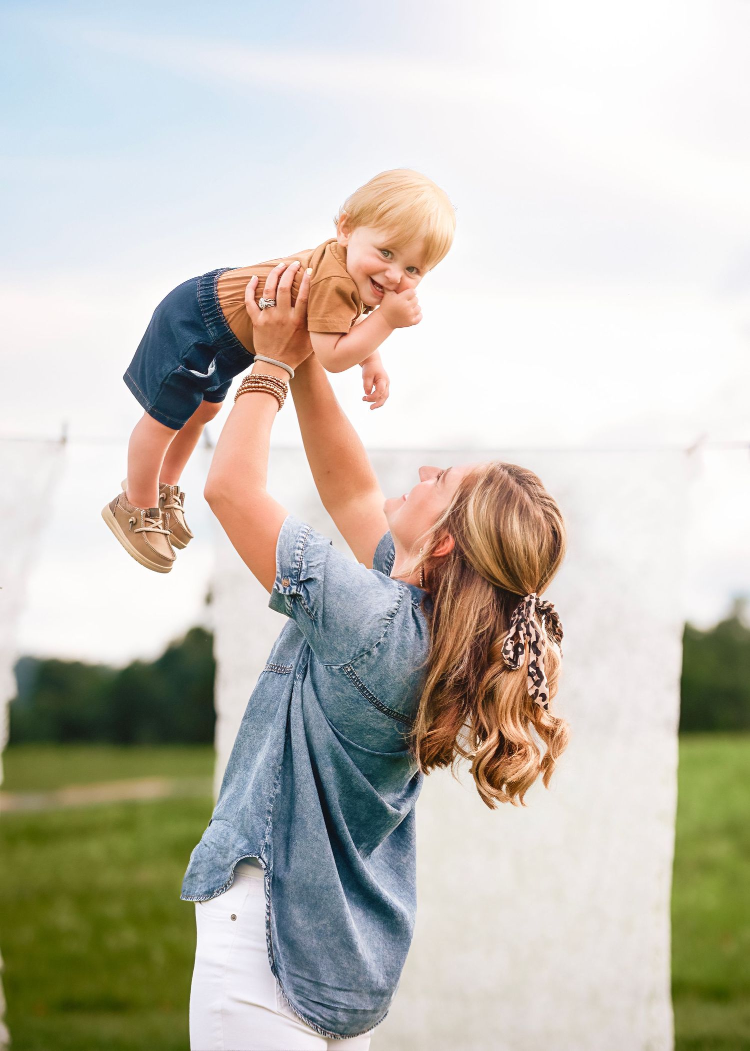 Parent lifting child playfully in air against cloudy sky background.