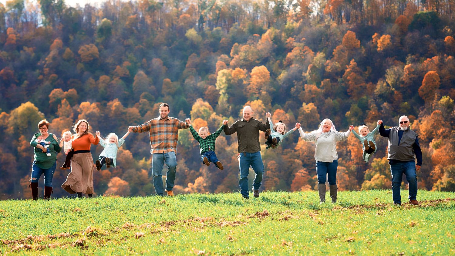 Wide panoramic view of a family photo session in a field with vibrant autumn colors in the background.