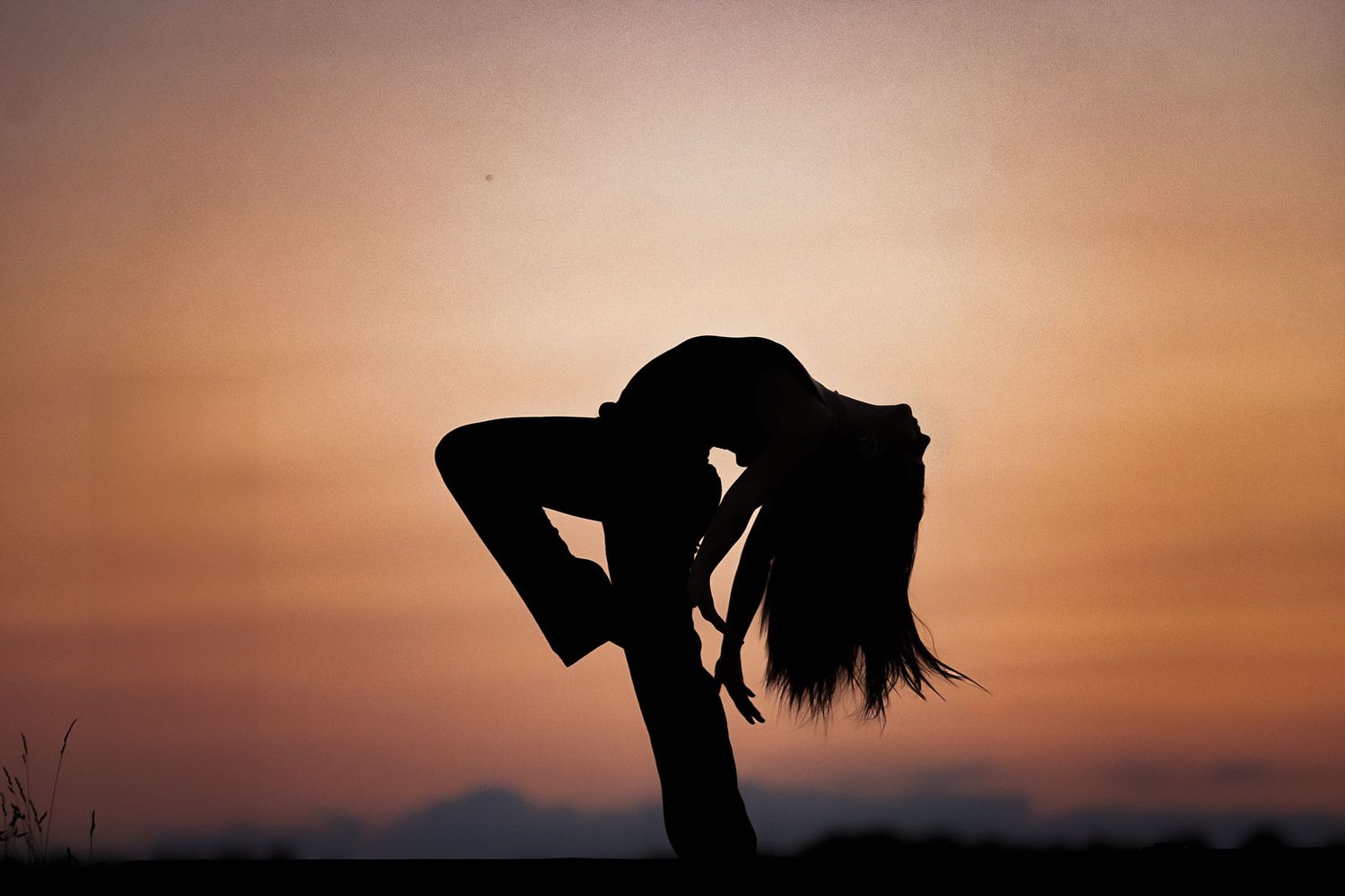 Silhouetted figure poses dramatically against an orange sunset sky.
