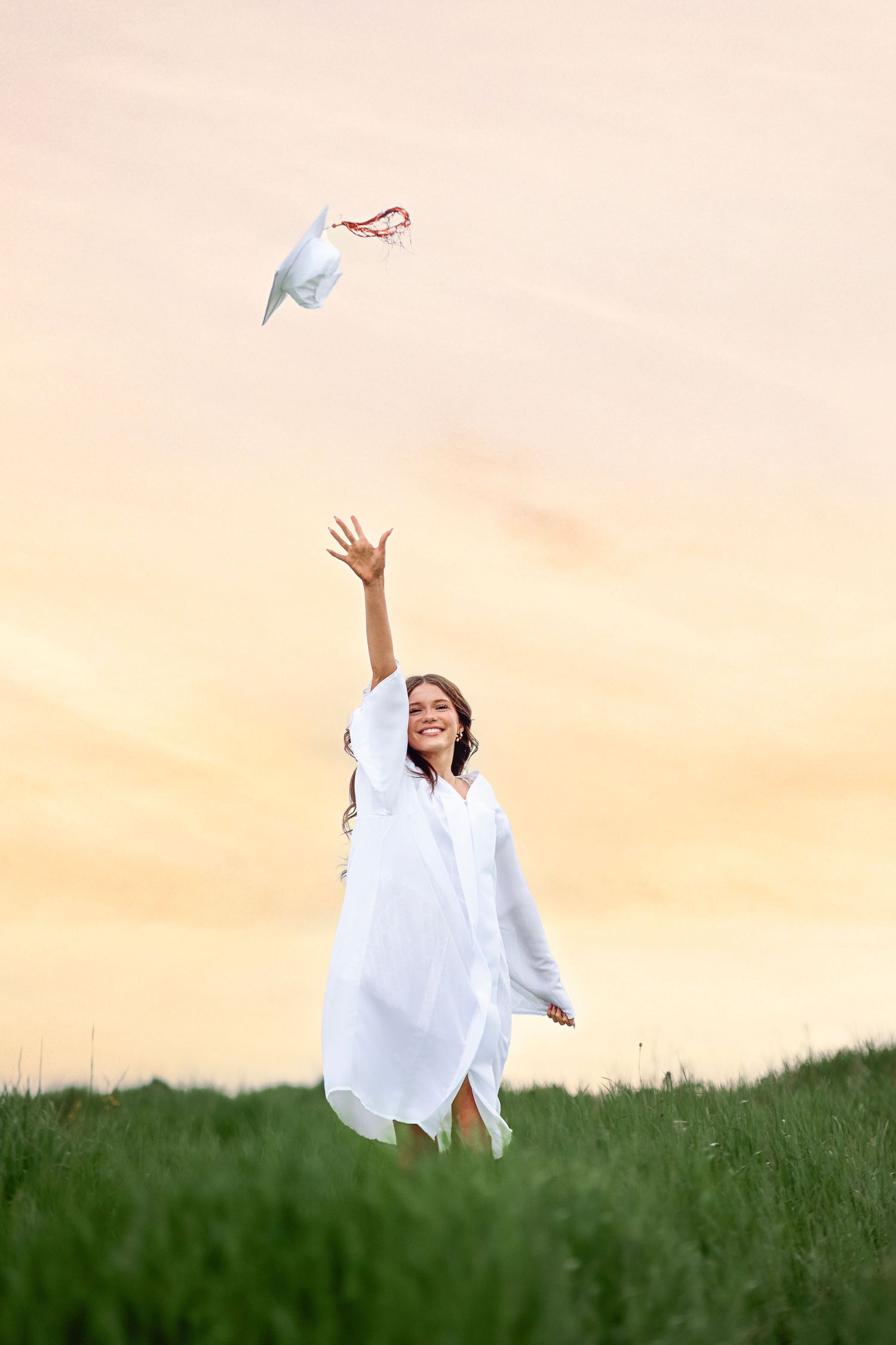 Person in white dress throws paper airplane against golden sunset sky.