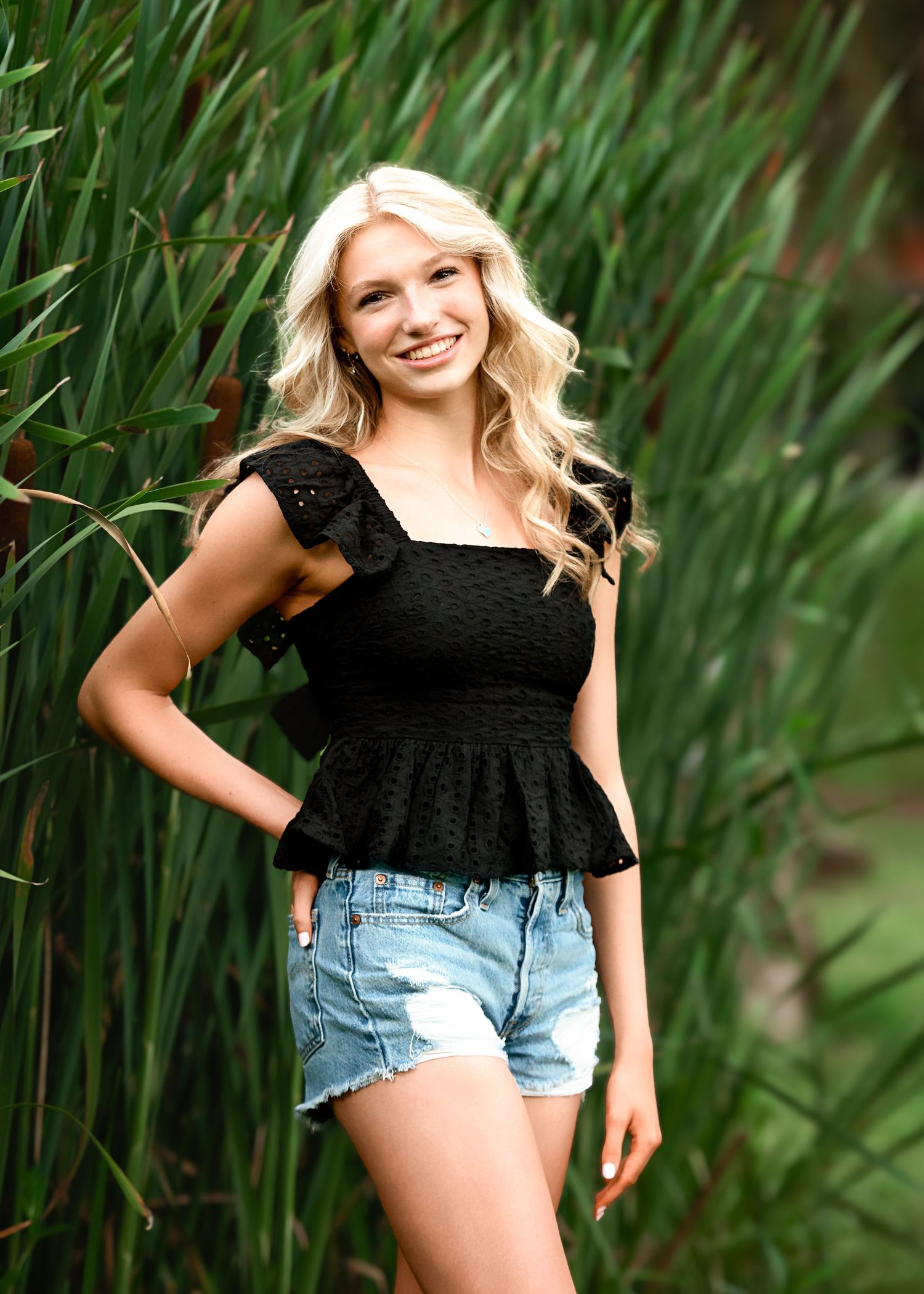 Black top and denim shorts outfit photographed against tall green reeds.