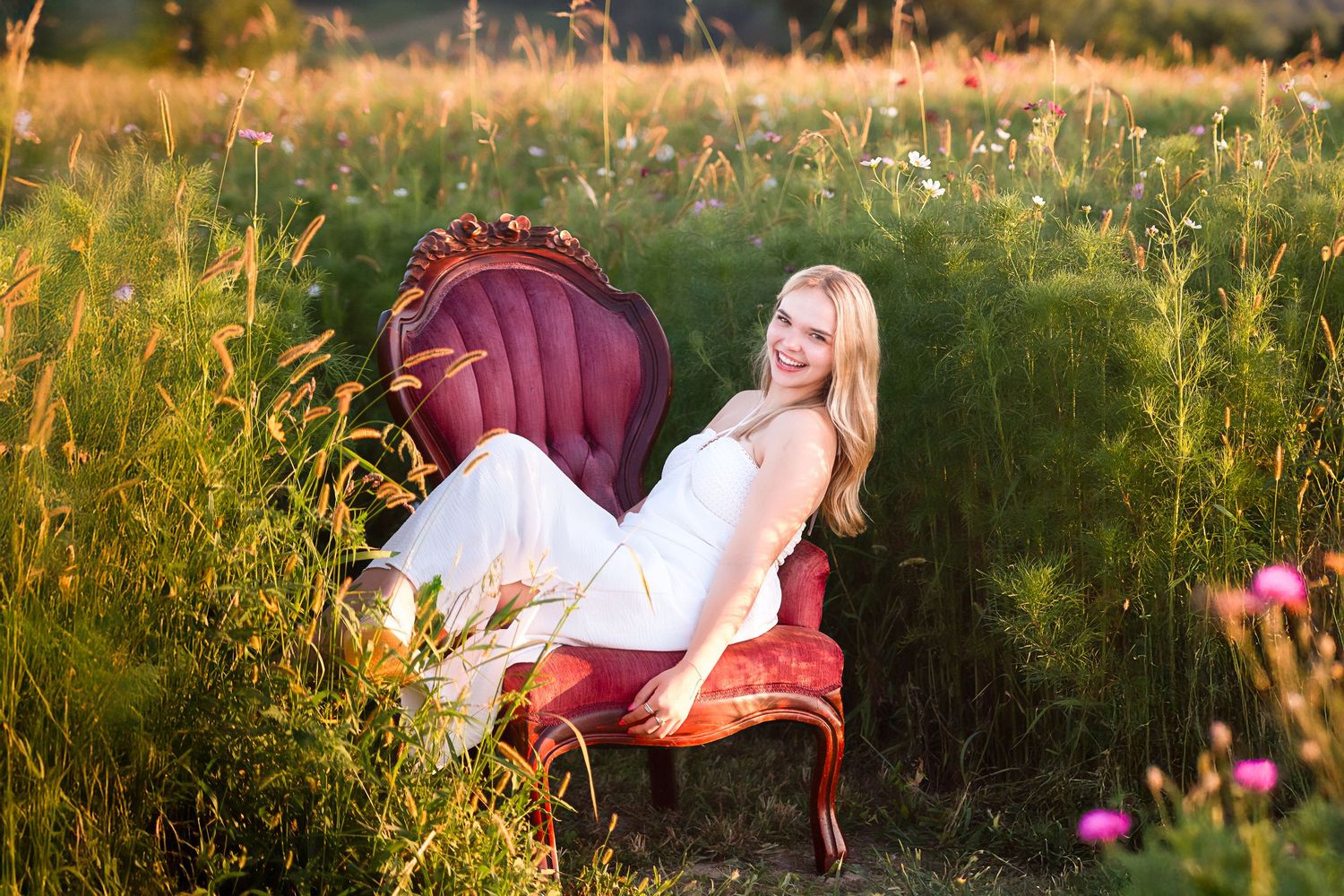 A senior poses in a golden field at sunset with tall grass surrounding them.