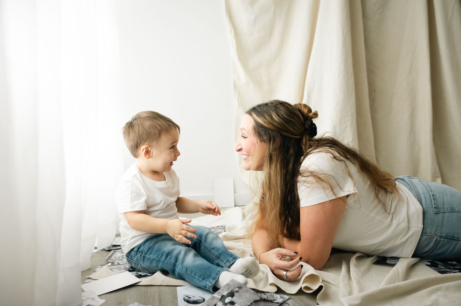 Mother and young child share playful moments together on a bed with white bedding.