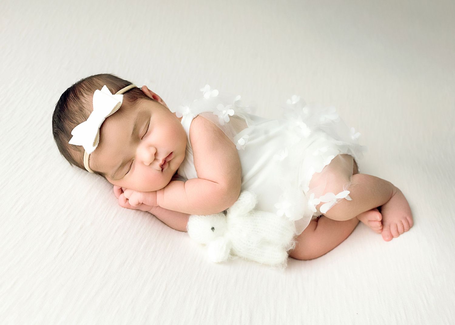 Newborn baby in white wrap sleeping peacefully on white textured background.