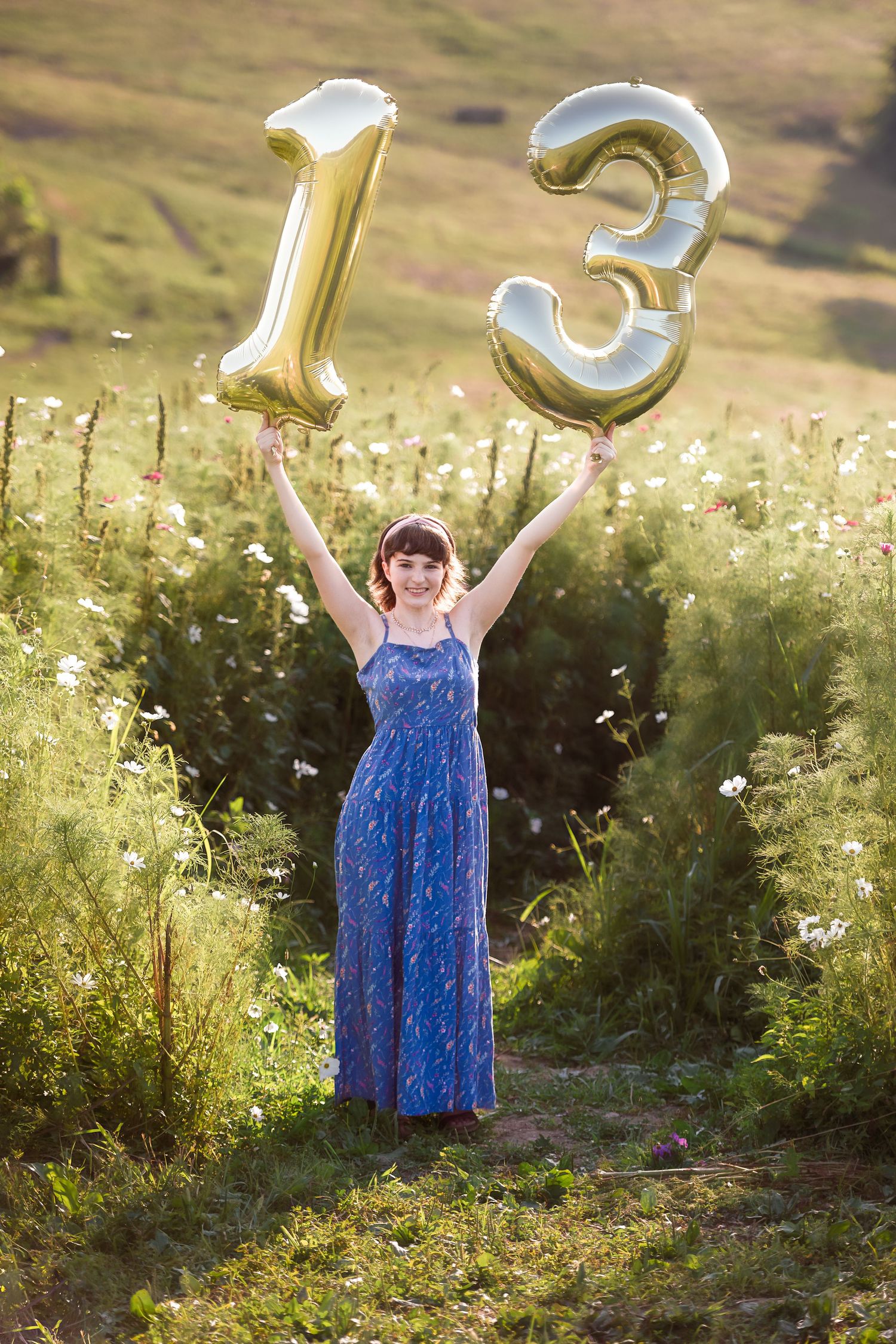 Gold number balloons in outdoor field with wildflowers during golden hour.