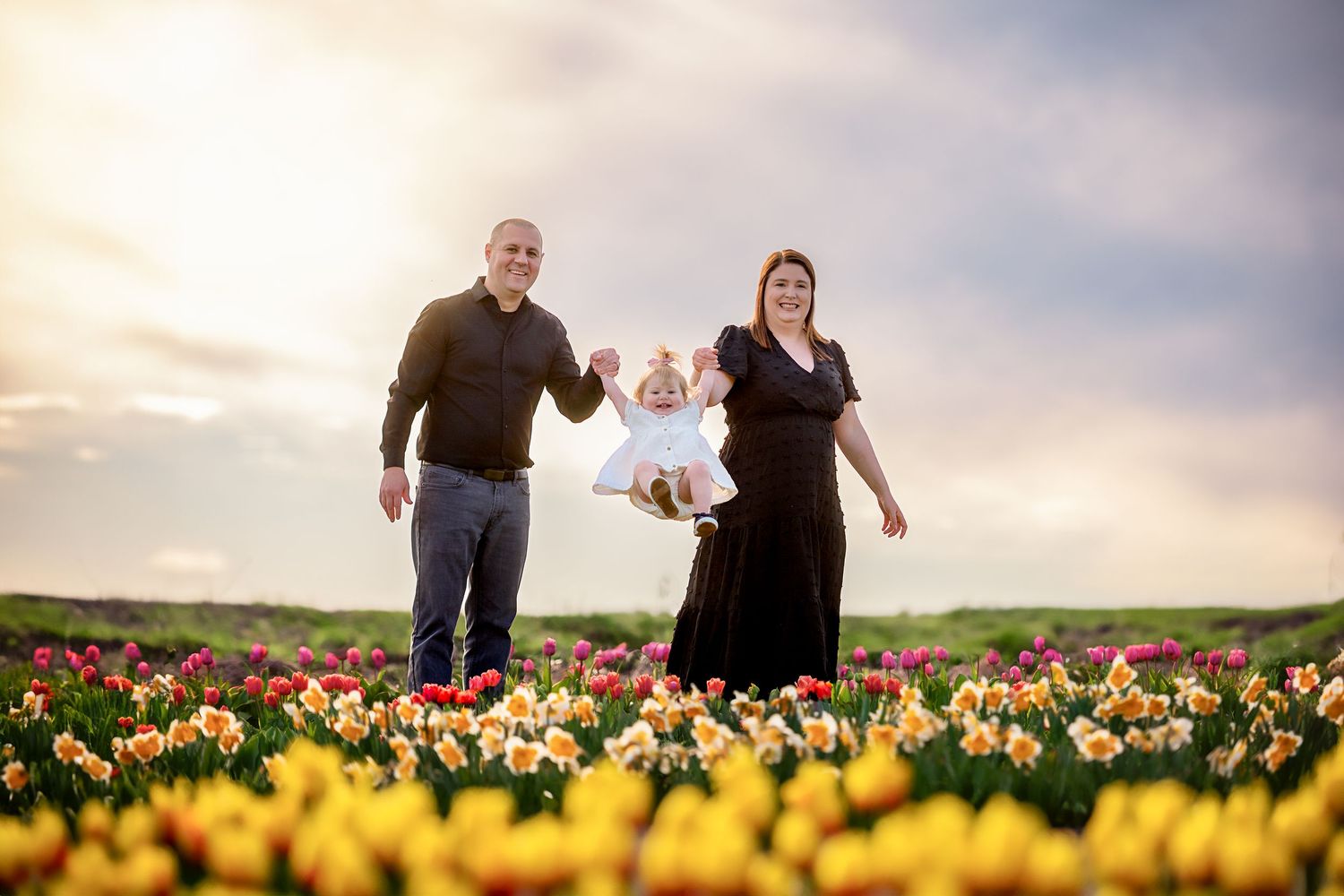 Family enjoying playful moments together in a vibrant tulip field at sunset.