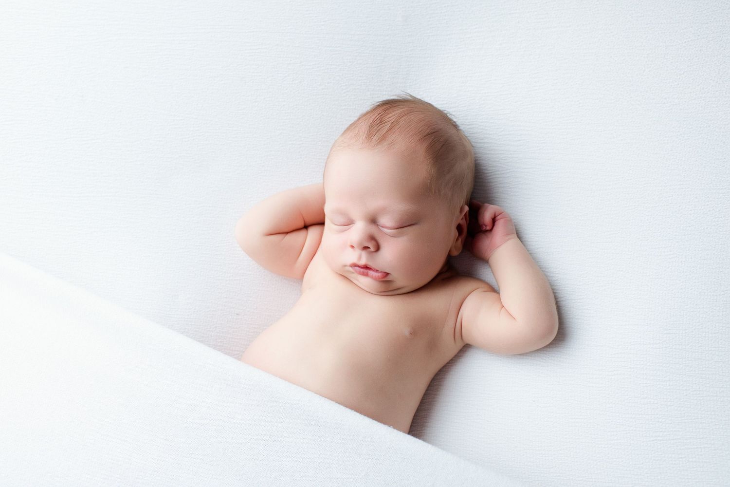 A sleeping newborn baby lying on soft white fabric in a minimalist style portrait series.