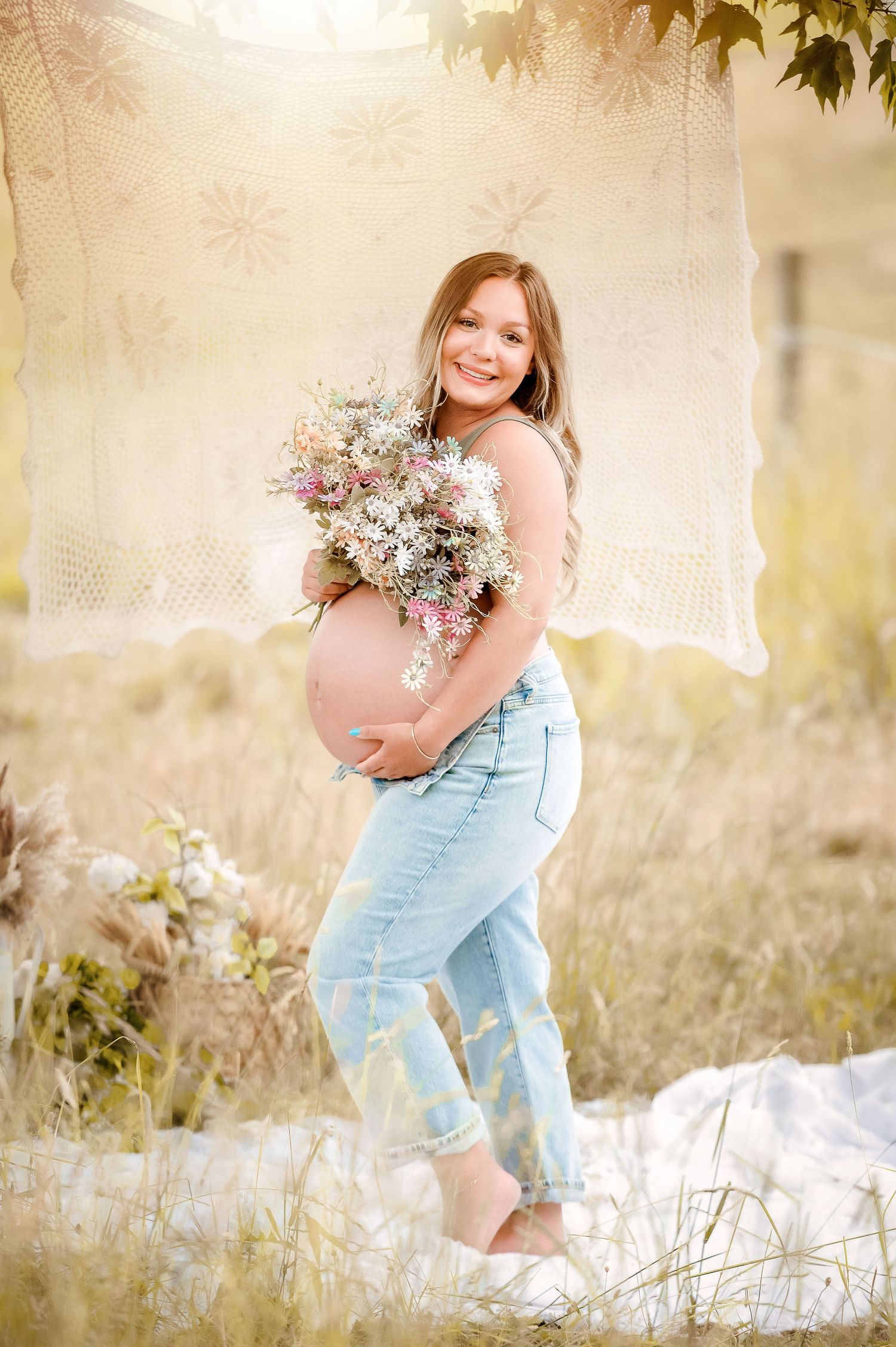Dreamy maternity portrait in a sunlit field with wildflowers.