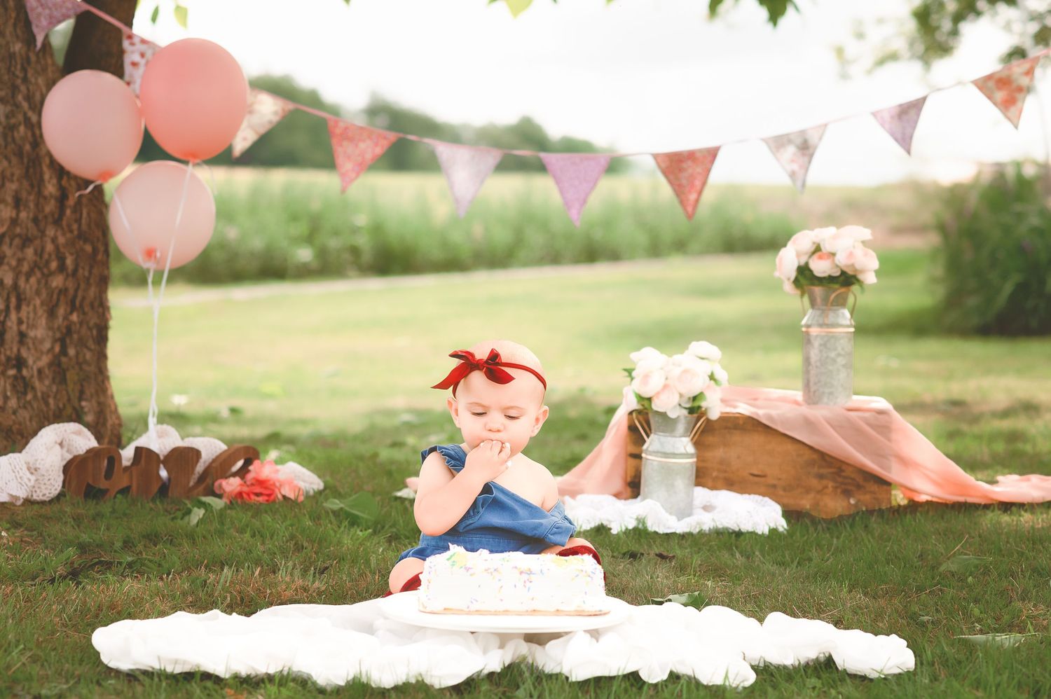 Outdoor party setup with pink balloons and bunting under trees.