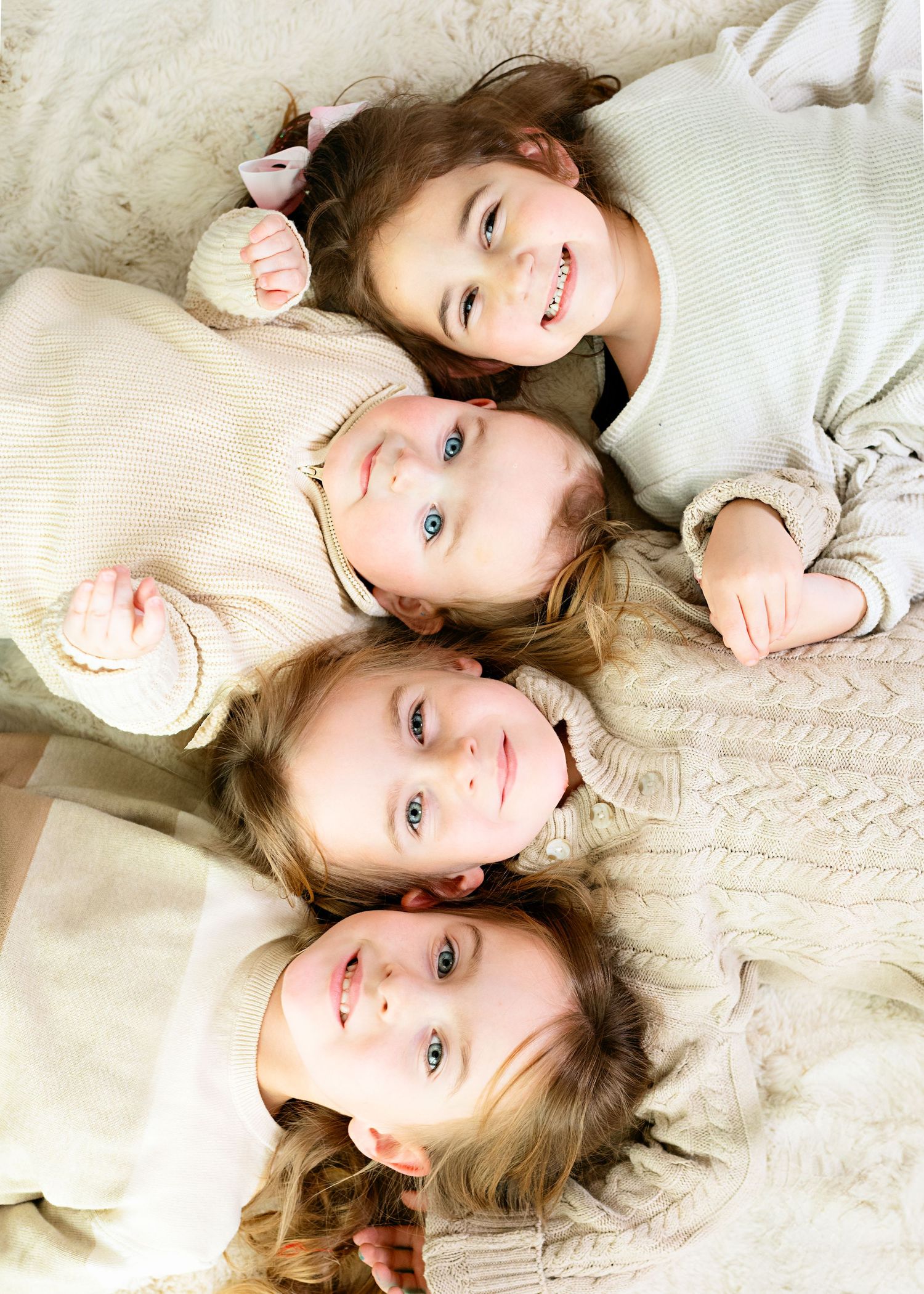 Overhead view of four siblings lying in circle wearing cream colored sweaters.