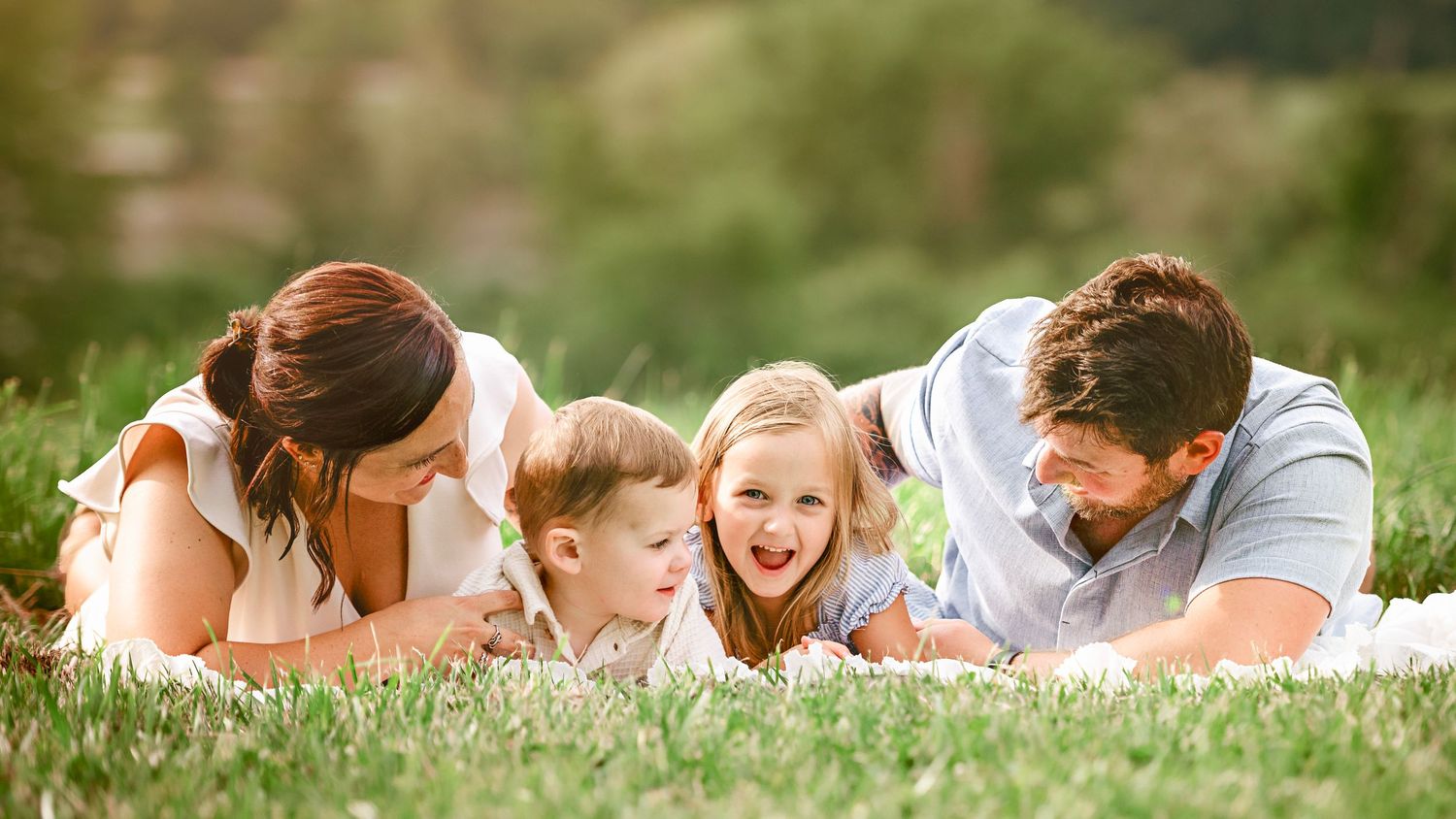 Playful family moments captured while laying in tall grass during a summer photo session.