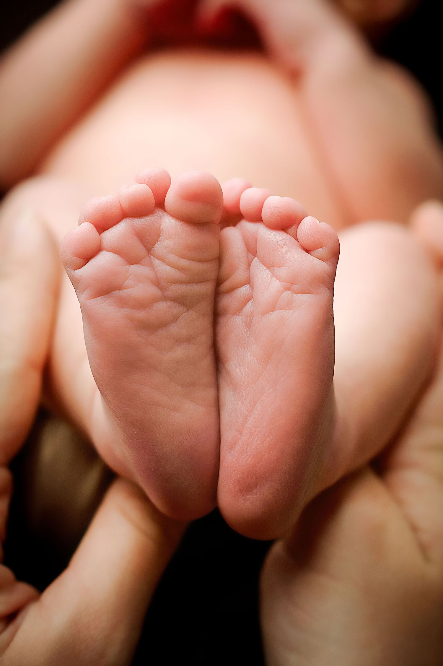 Close-up of tiny newborn feet held gently in hands against pink background.