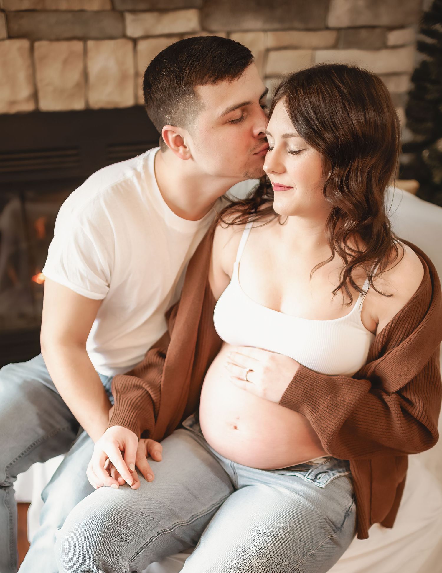 Intimate maternity photos of couple in casual wear sitting together indoors.