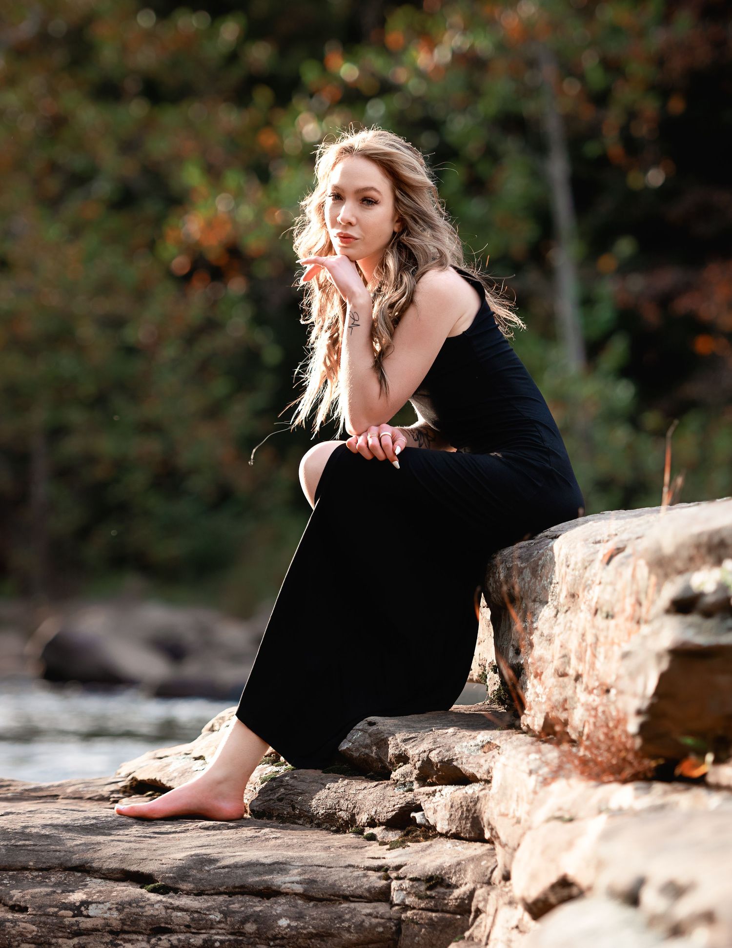 Person in black outfit reclining on rocky ledge in natural setting.