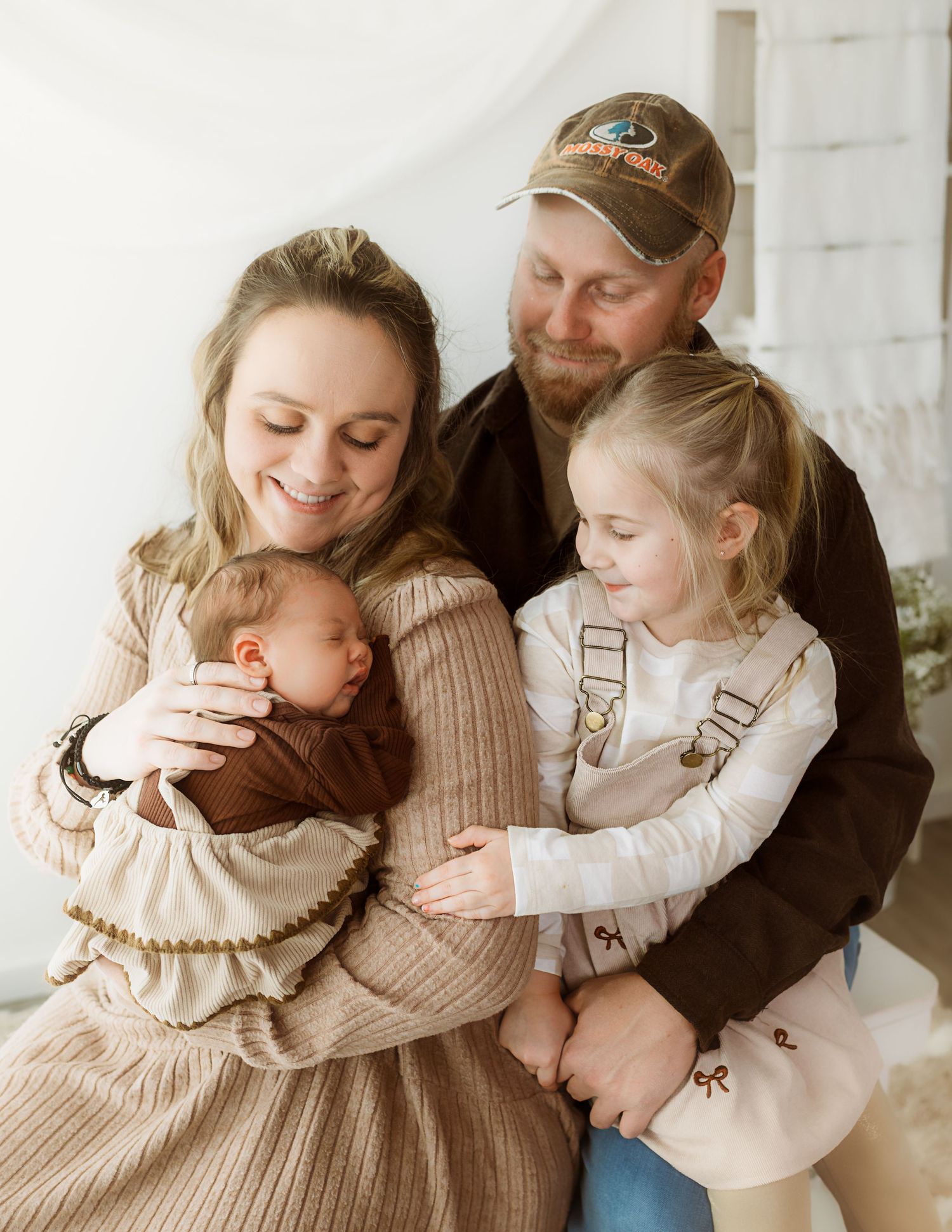 A family shares a tender moment together in neutral tones while sitting against a white wall.