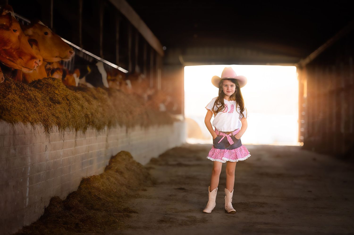 Silhouetted figure in cowgirl outfit standing in barn doorway with dramatic backlighting.
