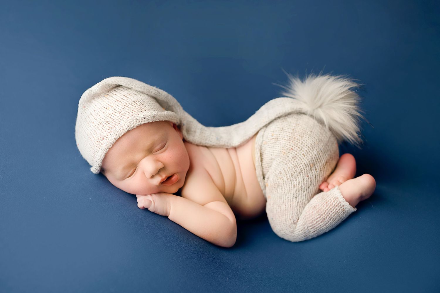 Artistic newborn photography series with baby posed against deep blue backdrop.