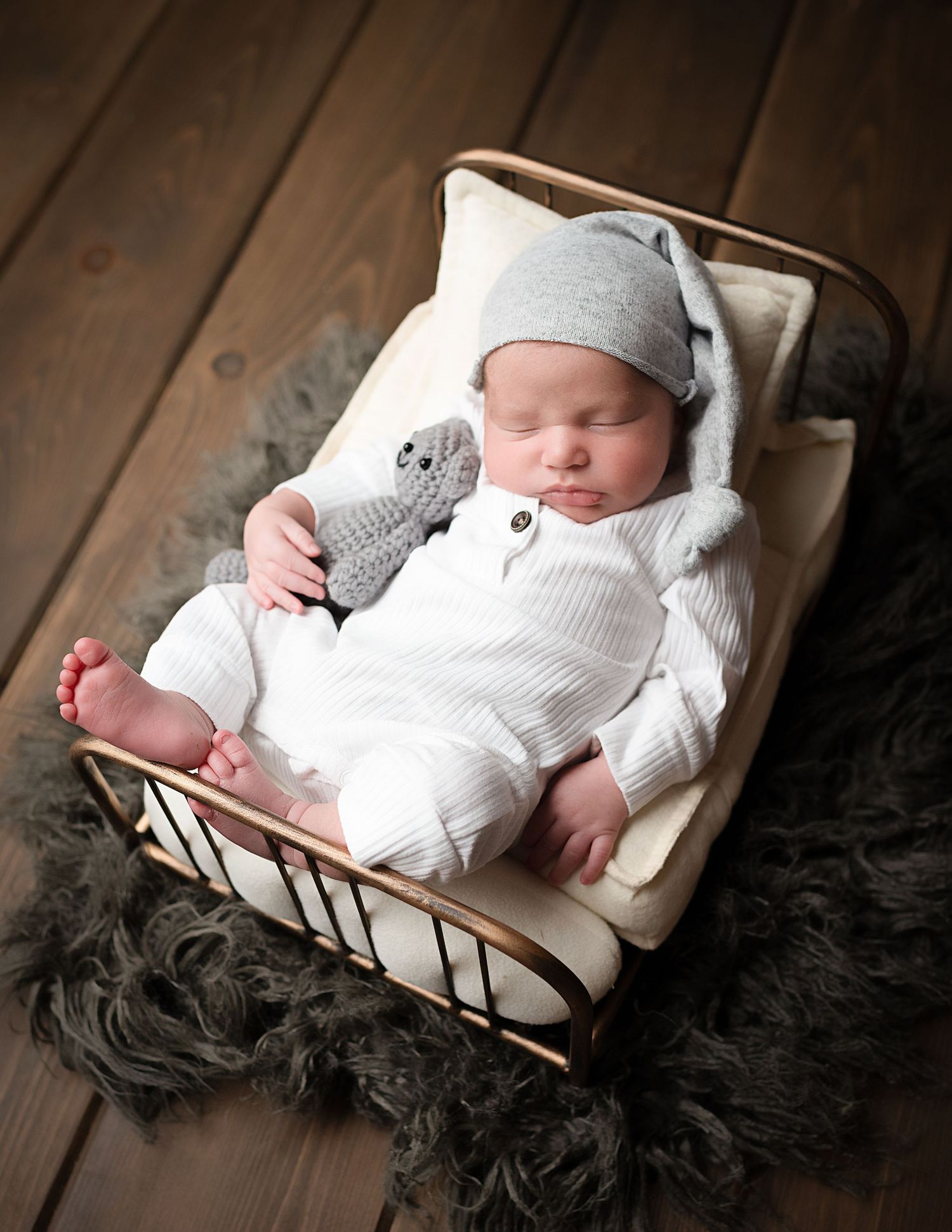 Baby dressed in white sleeps in vintage wooden crate with plush gray blanket.