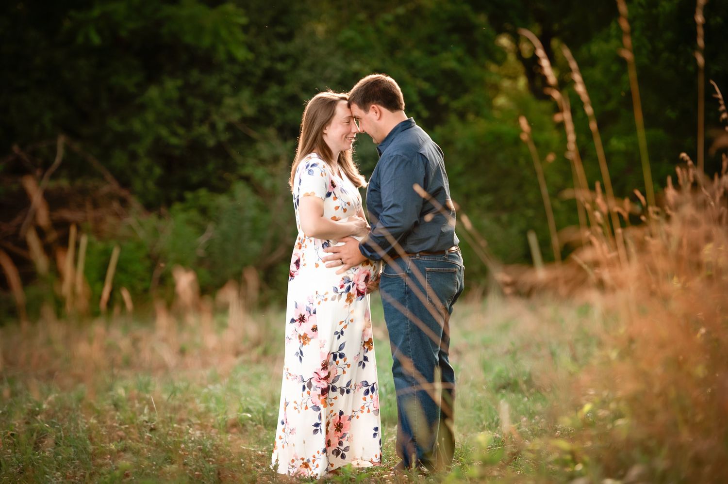 Couple embracing in a natural setting with tall grass during golden hour.