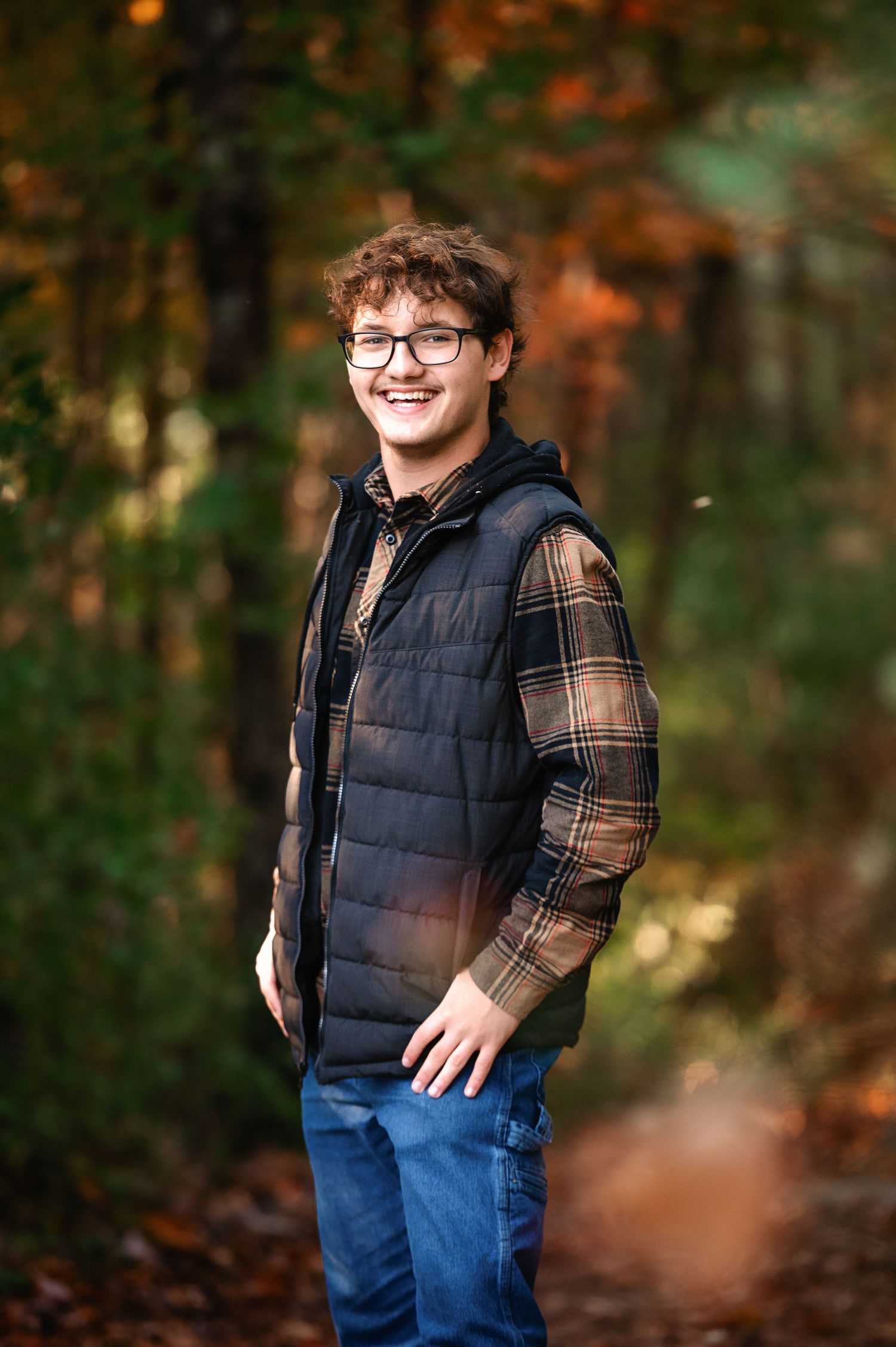 Fall portrait session featuring a puffy vest and plaid shirt in autumn foliage.