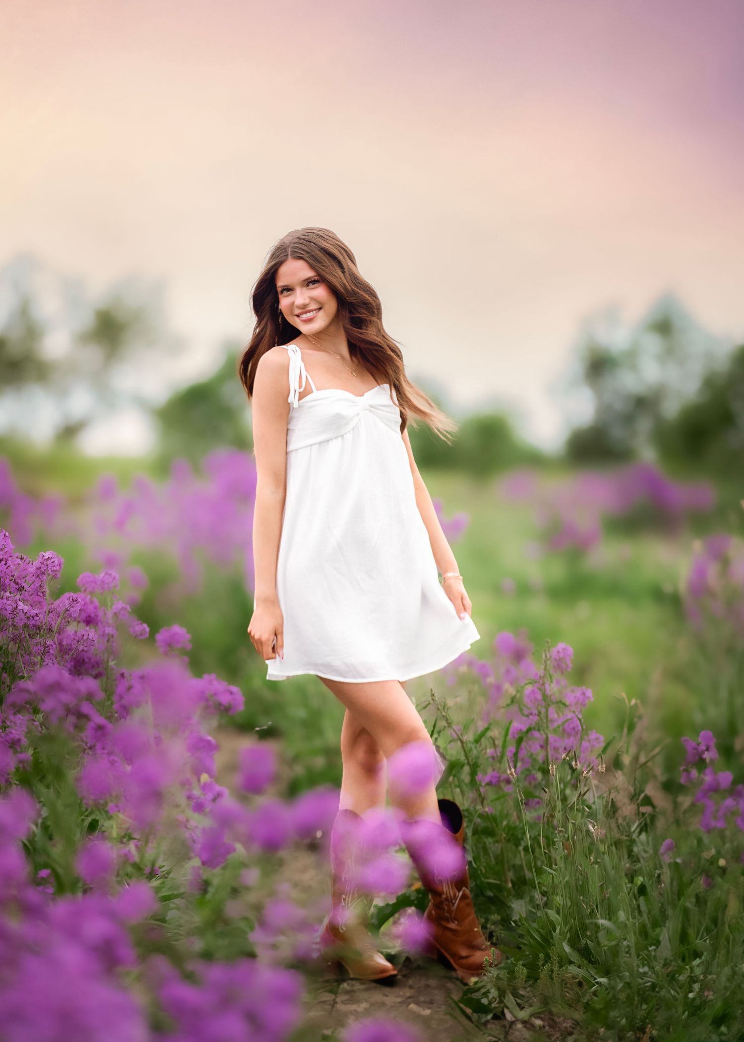 Woman in white dress stands among purple wildflowers in summer field.
