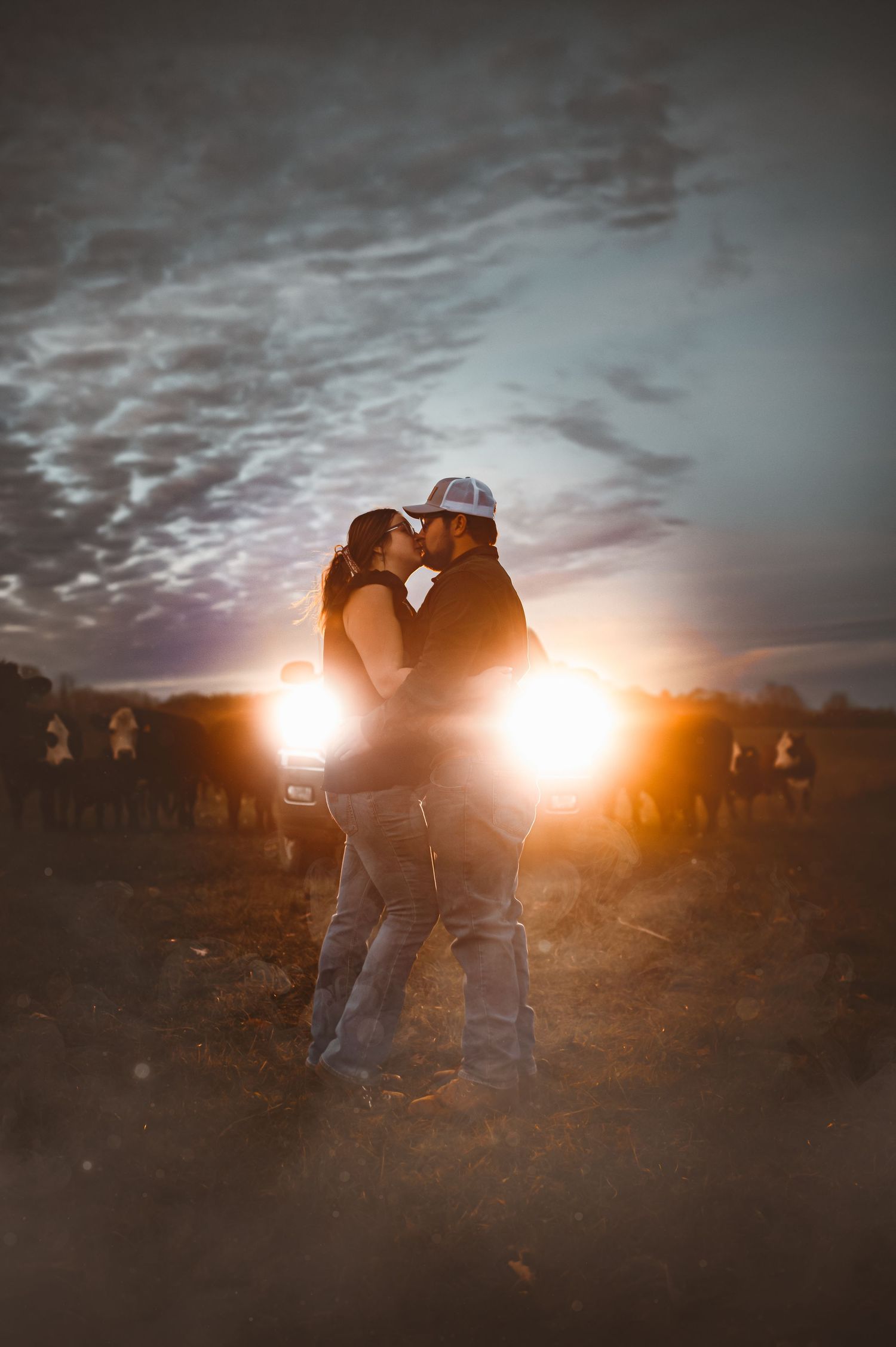 Silhouetted couple embraces against dramatic sunset sky with clouds creating romantic atmosphere.