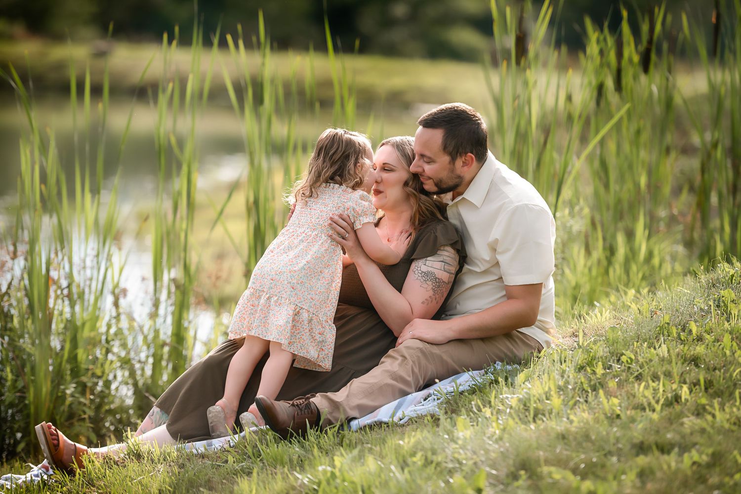 Intimate family moment captured in tall grass by a lake during sunset.
