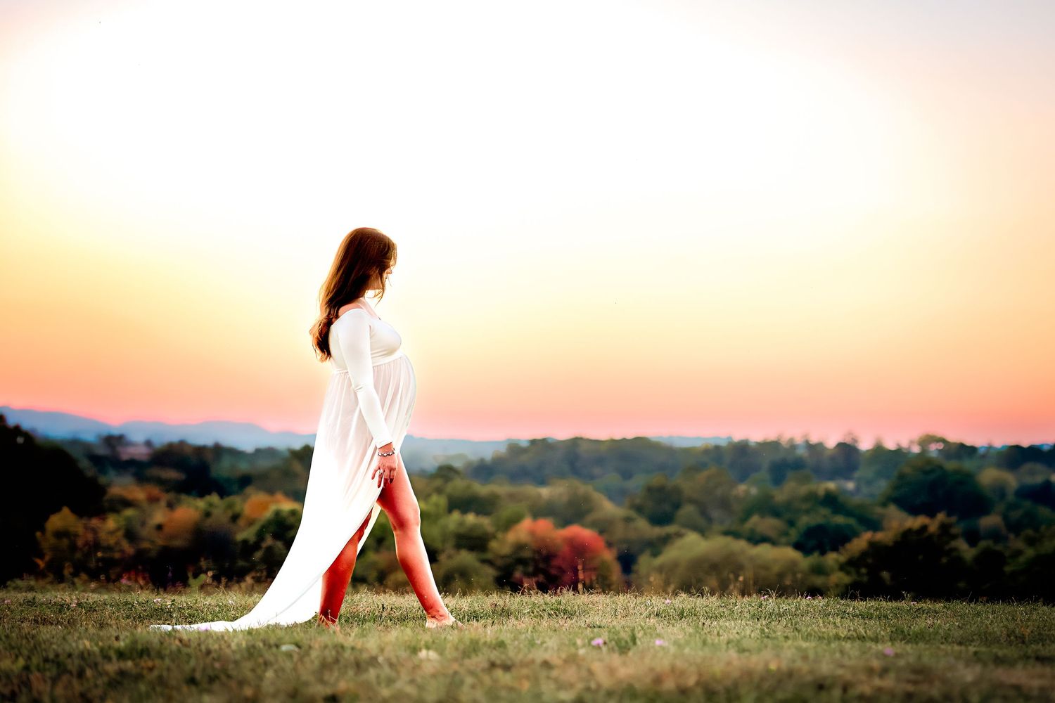 Dreamy sunset photography with flowing dress against pastoral landscape.