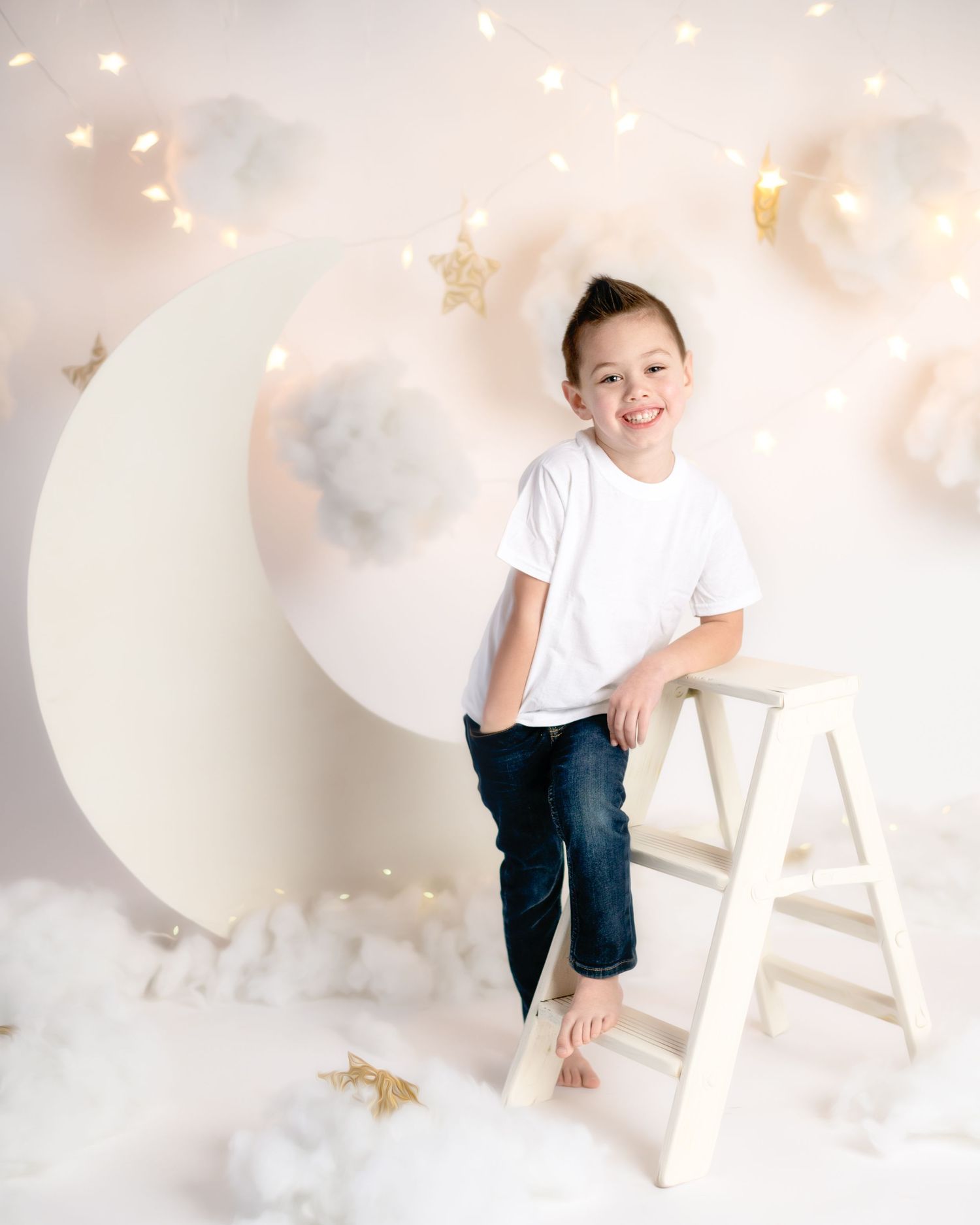 Dreamy moon and cloud backdrop with child on ladder in white shirt and jeans.
