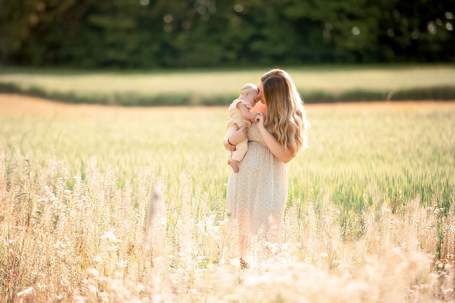 Couple walking through a sun-lit field with tall grass and wildflowers during golden hour.