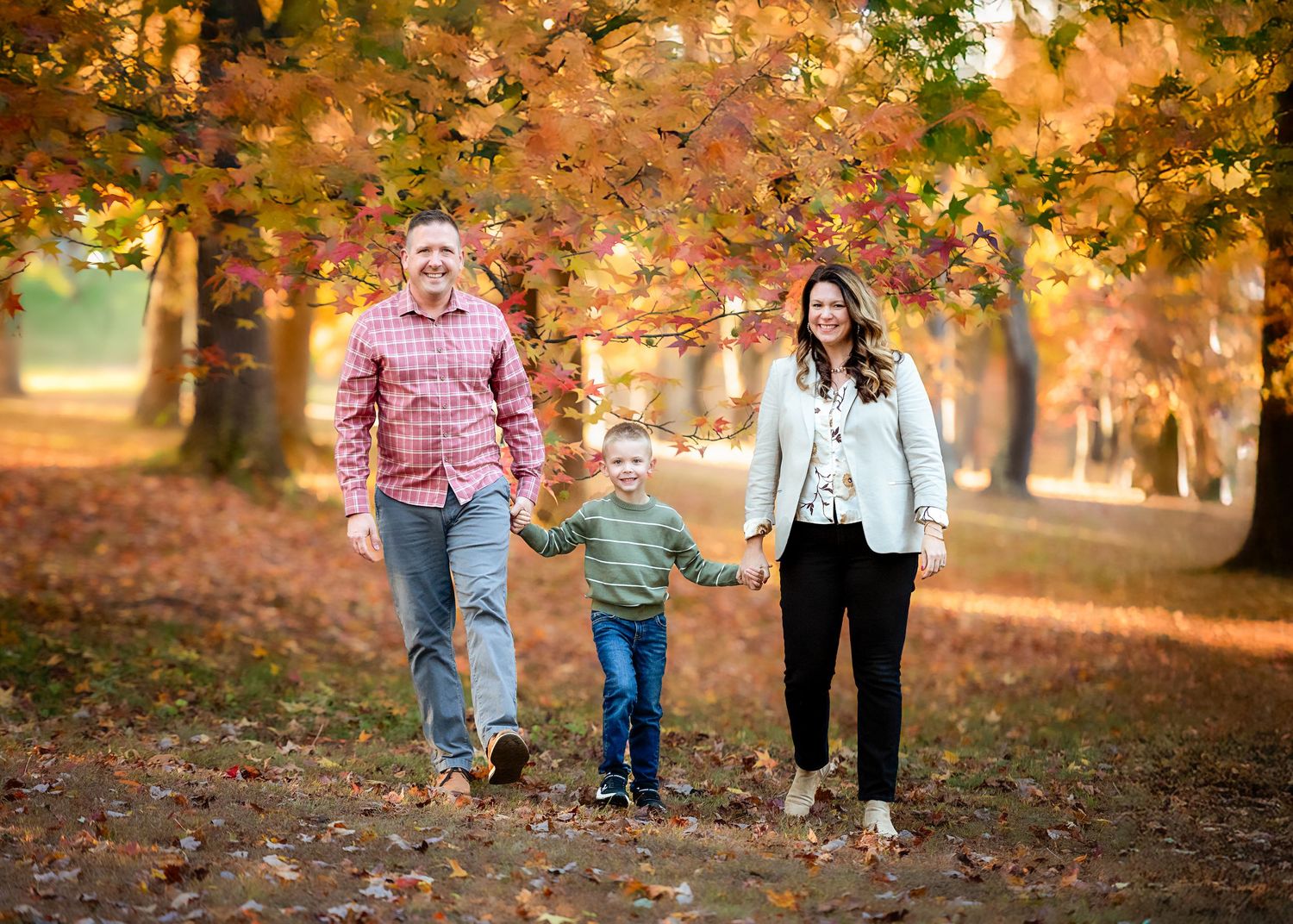 Family playing together in a park filled with golden autumn leaves during sunset.