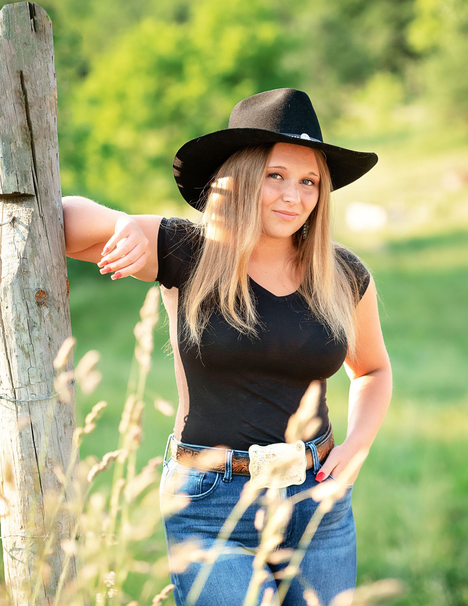 Woman in black top and jeans poses outdoors in a grassy field during golden hour.