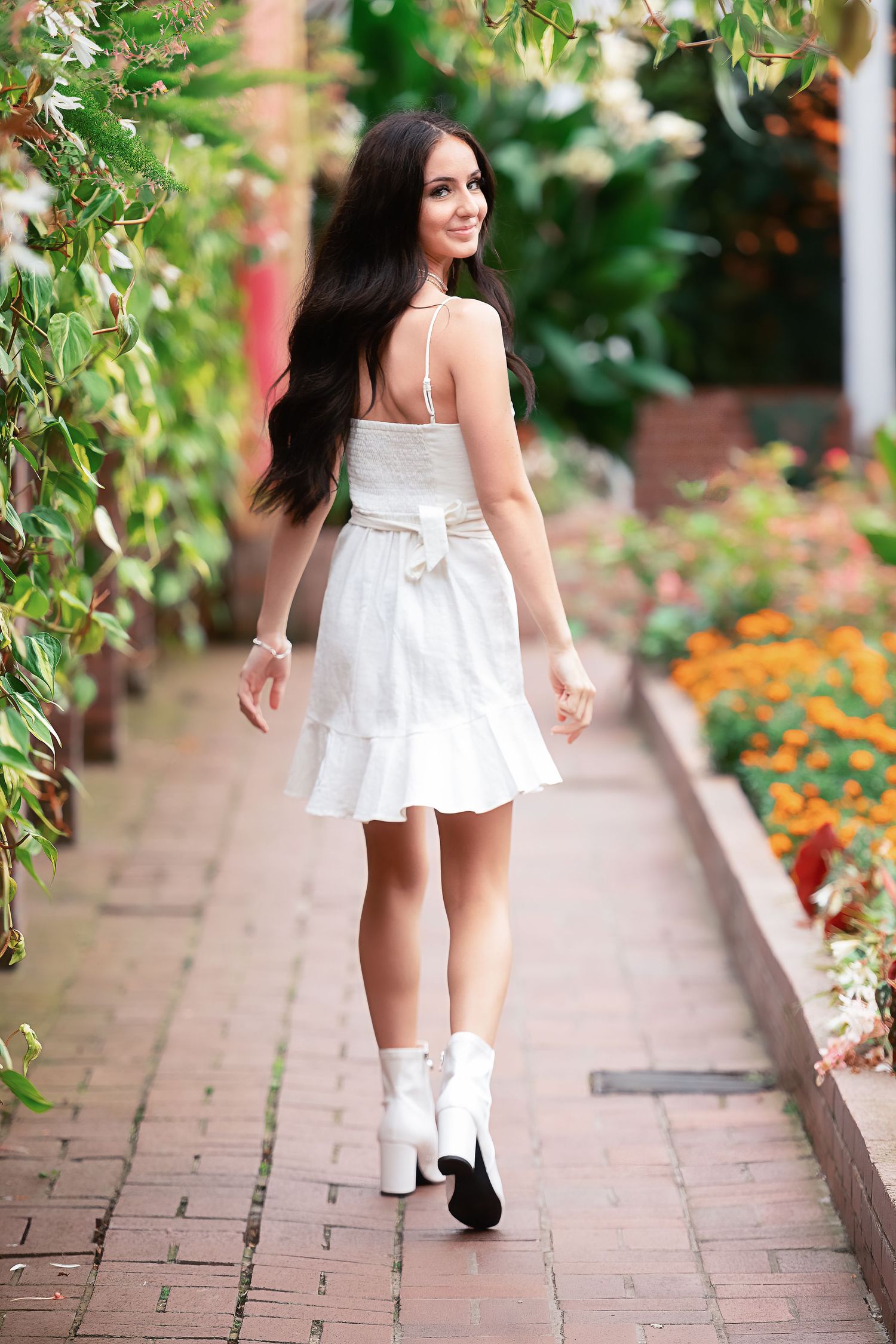 A white sundress photoshoot along a brick pathway lined with colorful flowers.
