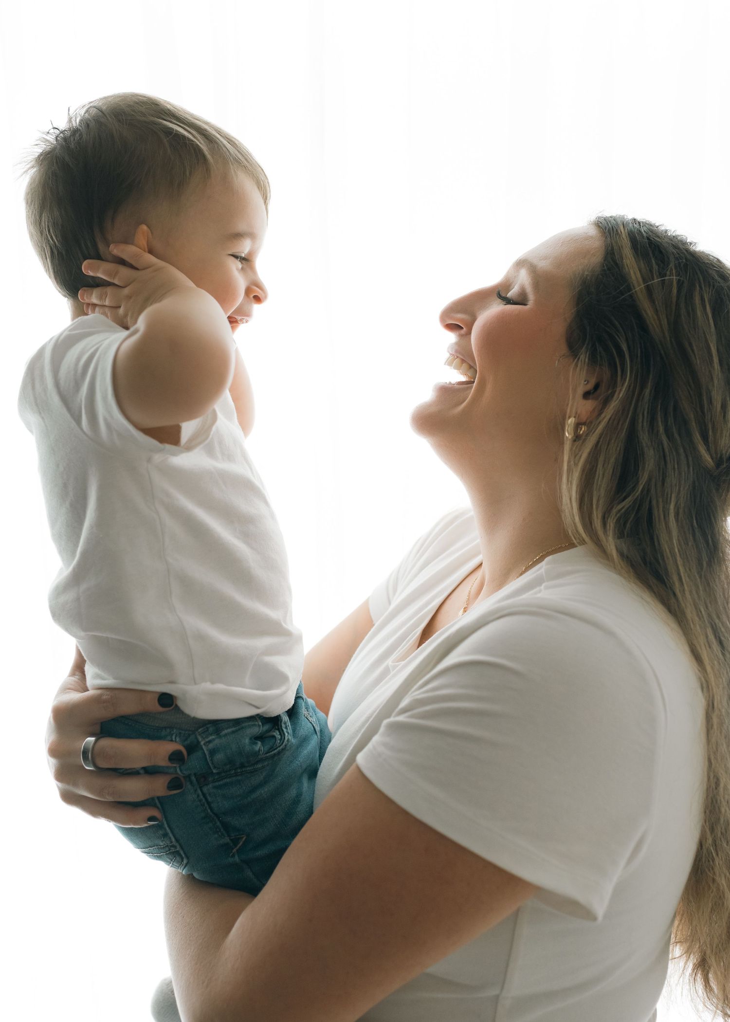 A parent holds a small child in a white shirt against a light background in a series of tender poses.