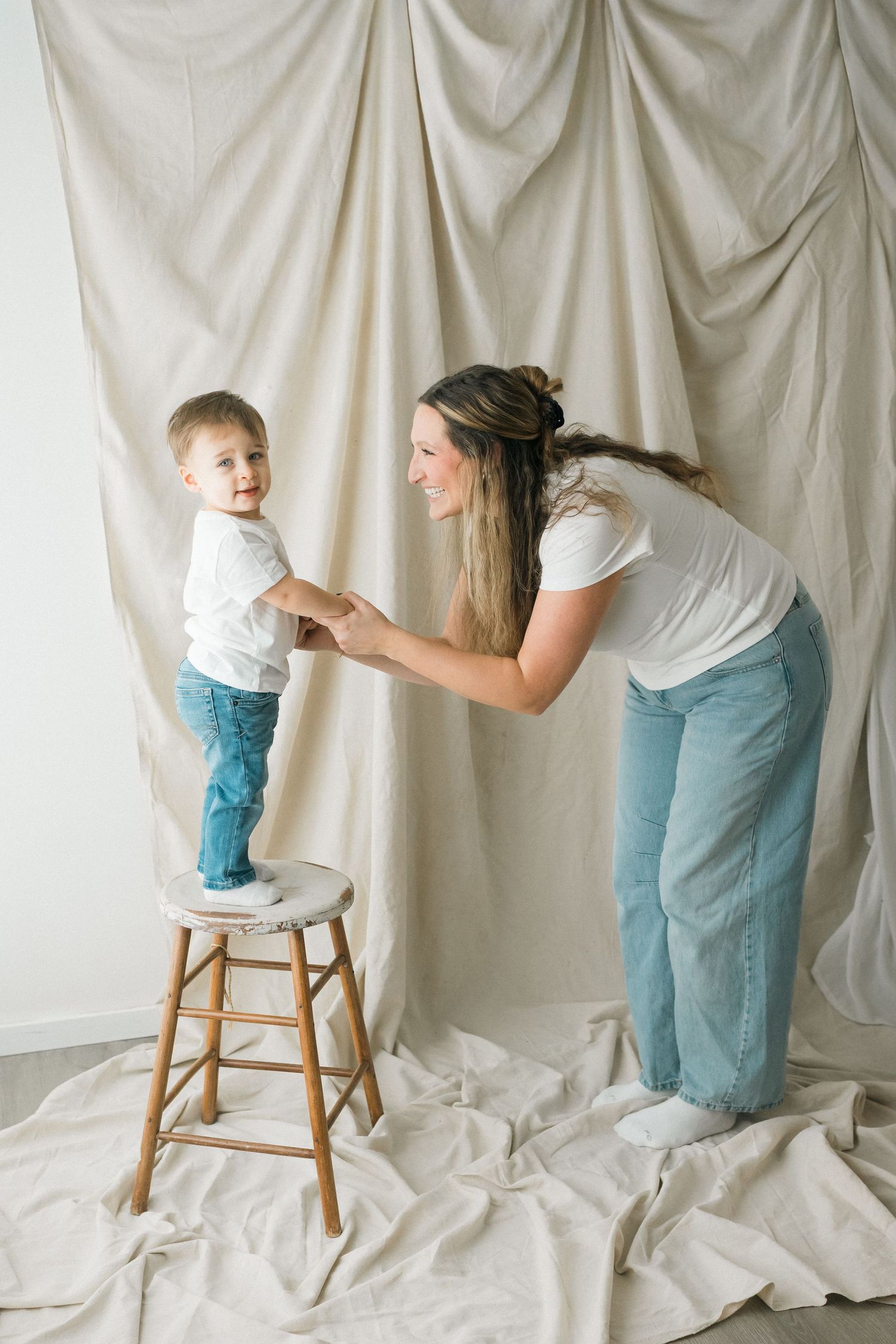 A tender moment captured against a white backdrop as a child stands on a wooden stool while an adult provides support.
