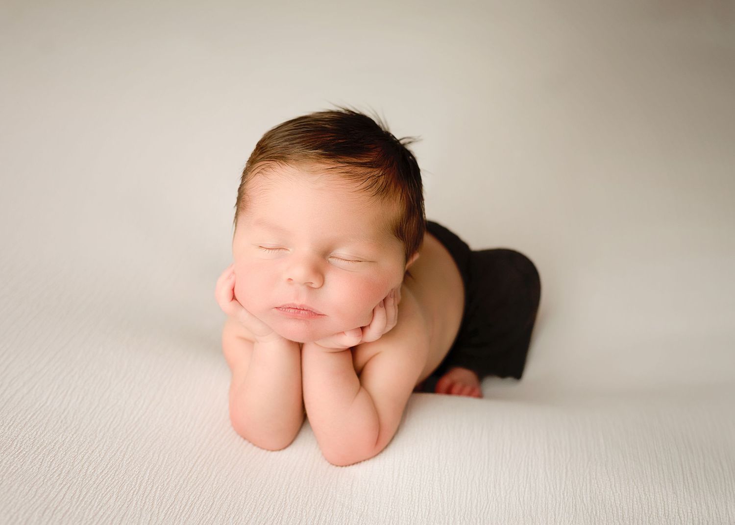A series of minimalist newborn baby portraits on white textured fabric showing tiny feet and curled up sleeping poses.