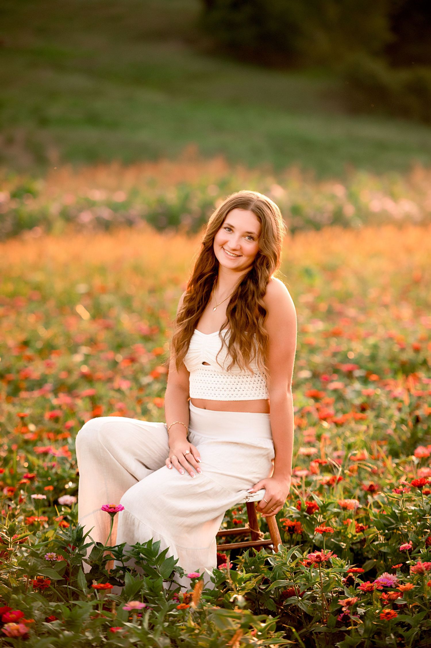 Elegant poses in a white dress among blooming red flowers at sunset.