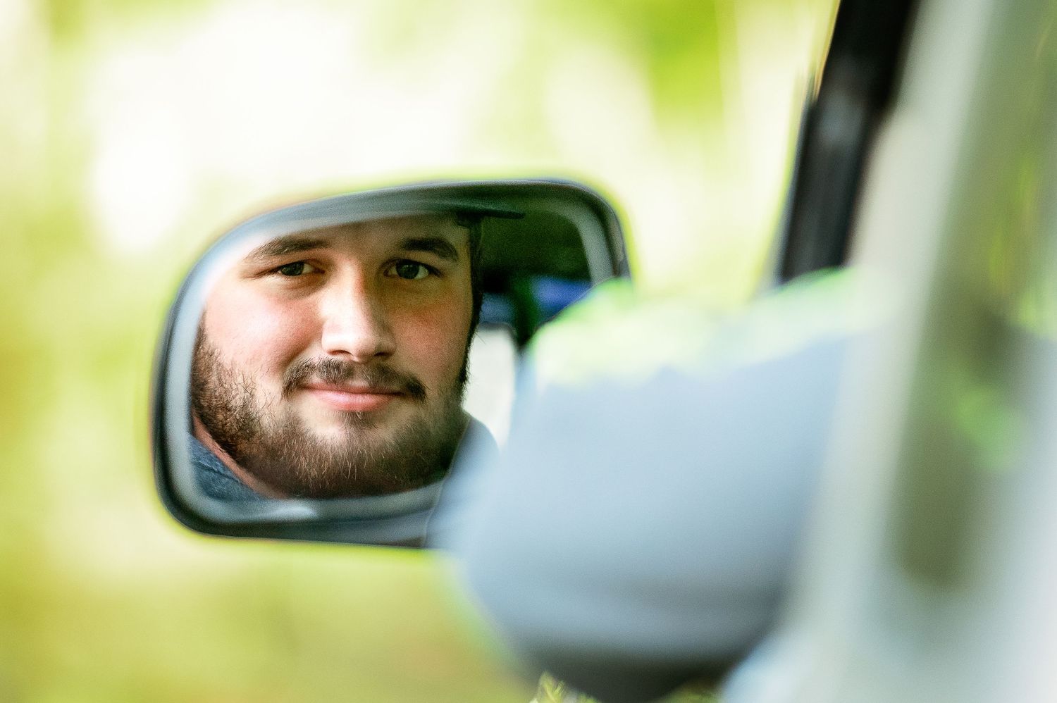 Close-up view of someone sitting in car with green blurred background.