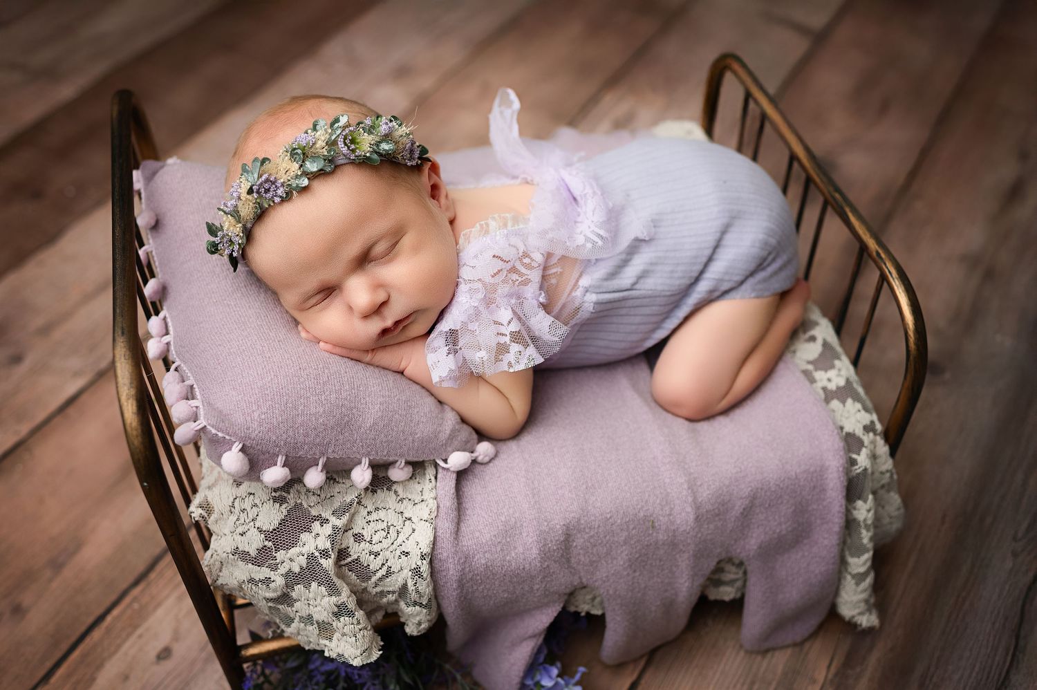 Sleeping newborn rests peacefully on purple elephant pillow in vintage metal bed with floral accents.