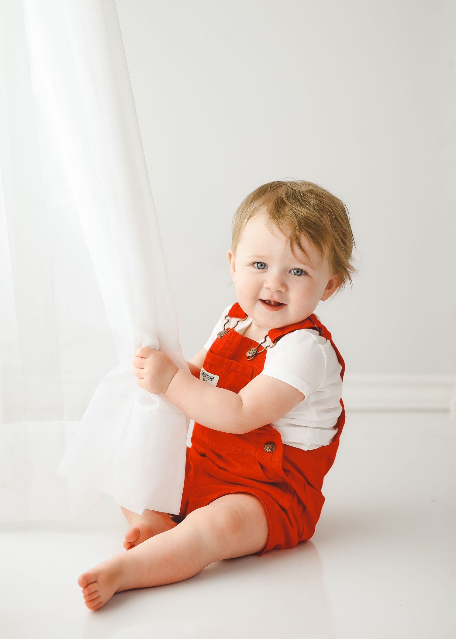 Baby in red outfit lying on white floor showing playful poses.